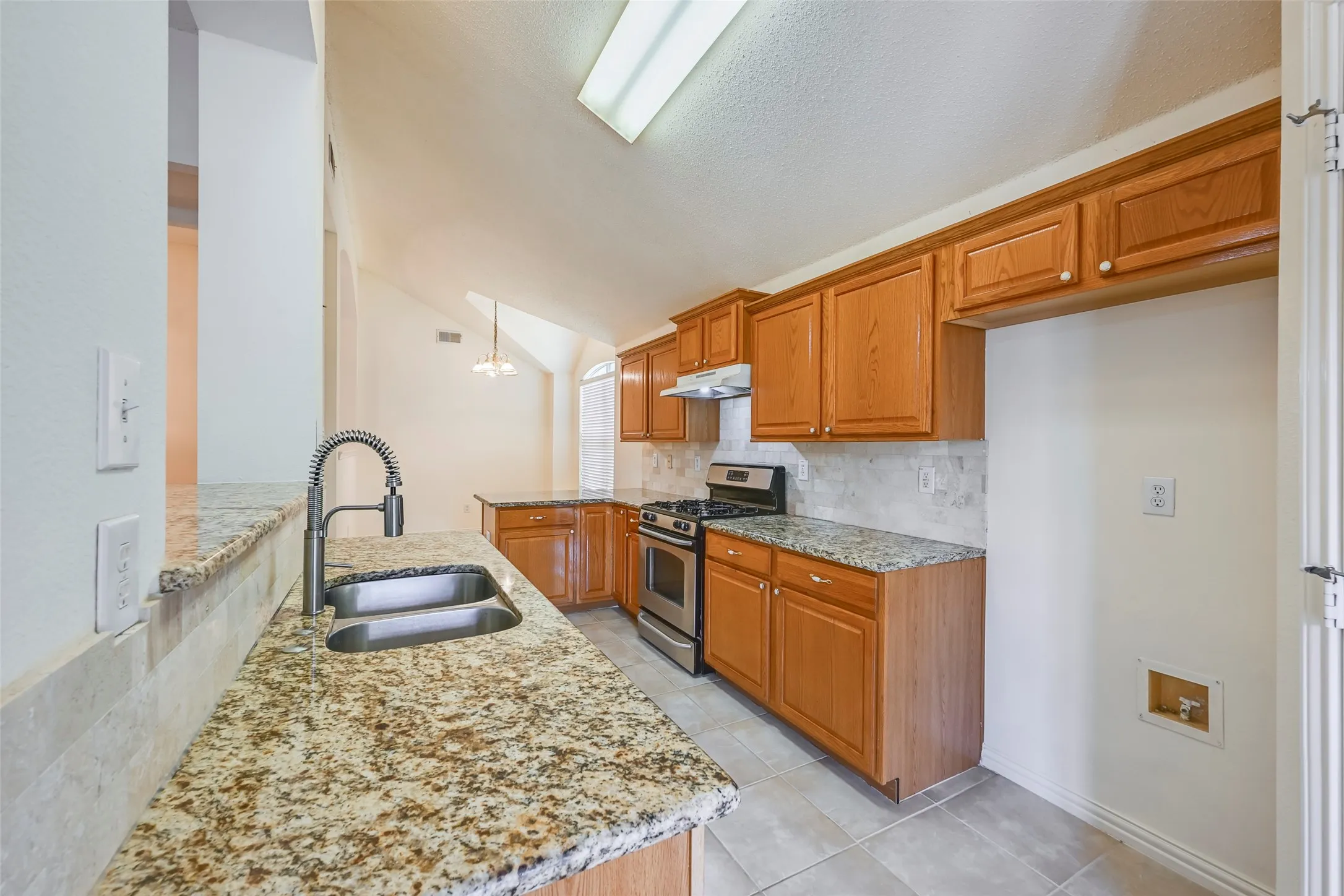 Kitchen featuring granite countertops, wood cabinetry, stainless steel appliances, and a vaulted ceiling with skylight