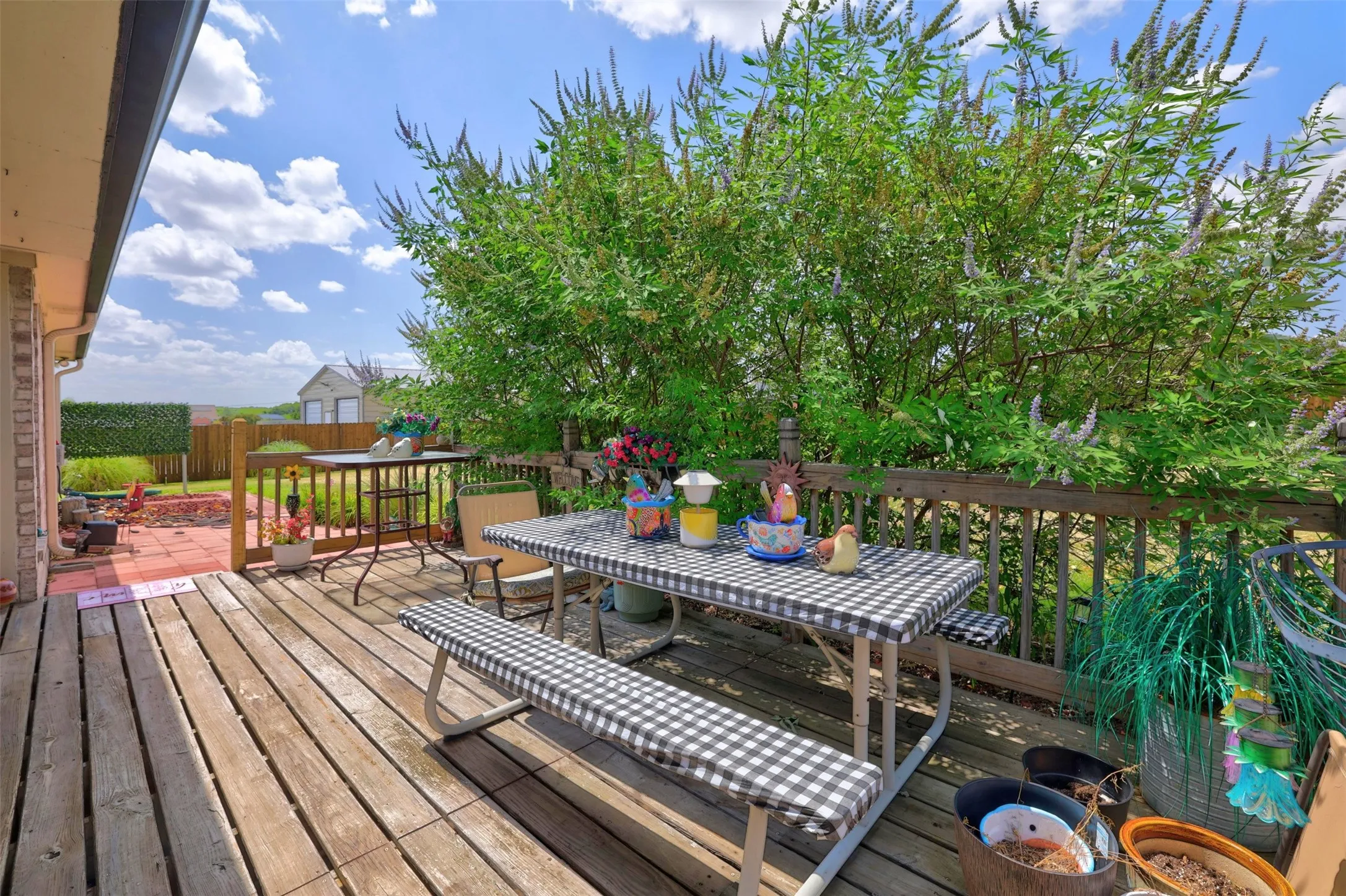 Expansive wood deck with a perimeter railing, mature shrubbery, and a red brick patio area