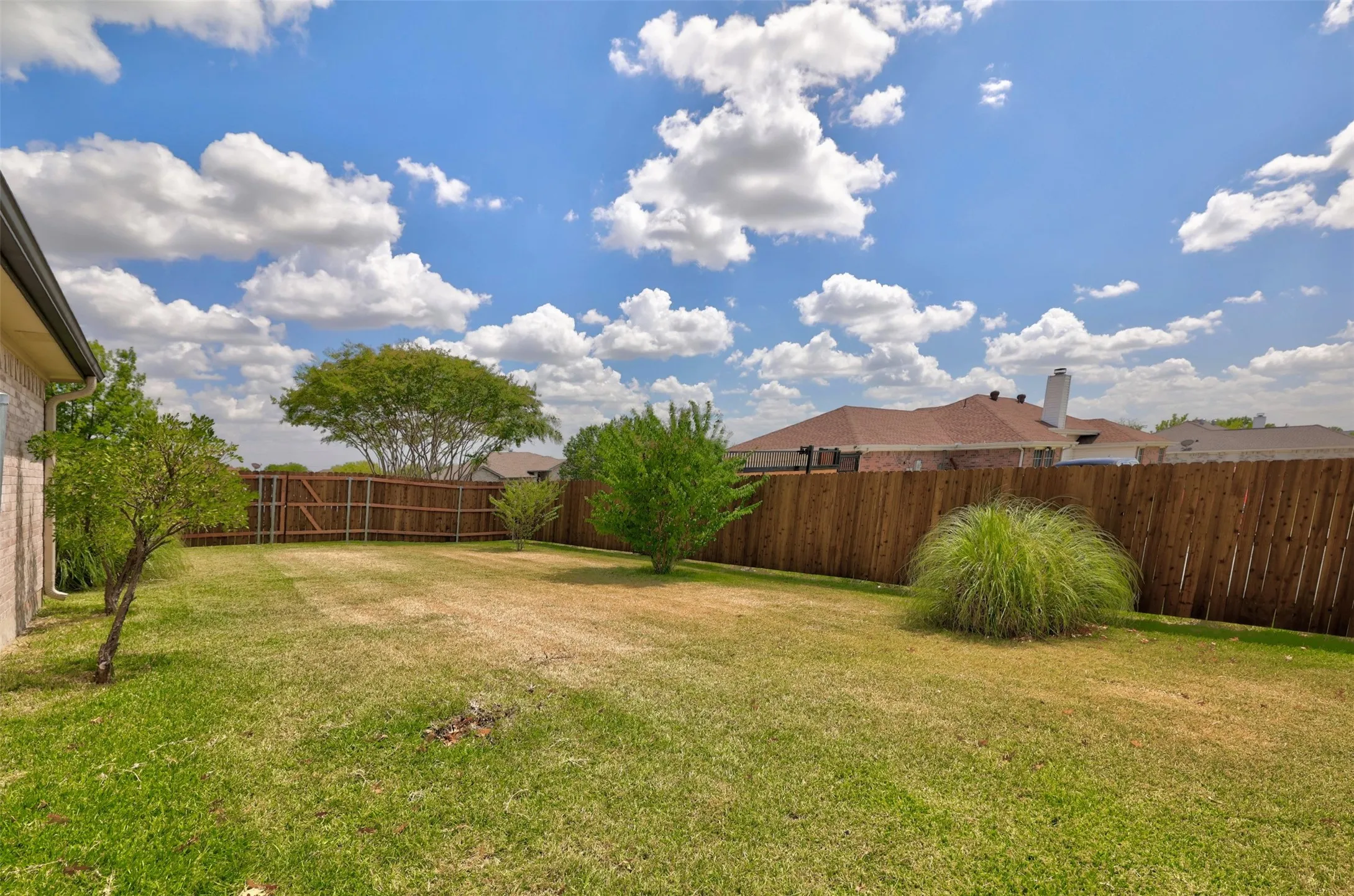 Expansive side lawn area enclosed by a new wooden privacy fence, featuring beautiful mature landscaping