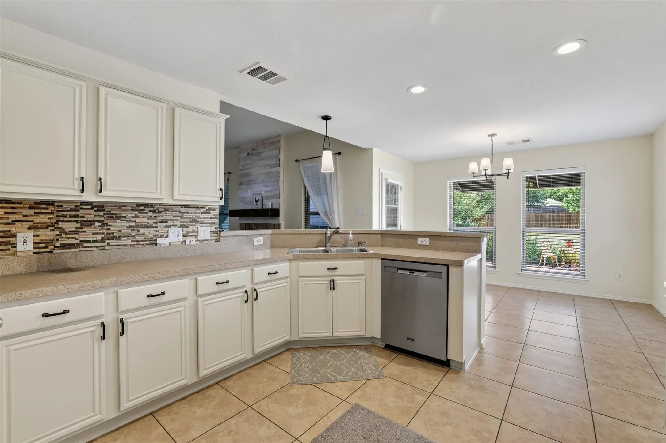 Beautiful cream cabinetry with matte black hardware, mosaic tile backsplash, stainless steel dishwasher, recessed lighting, and tile flooring
