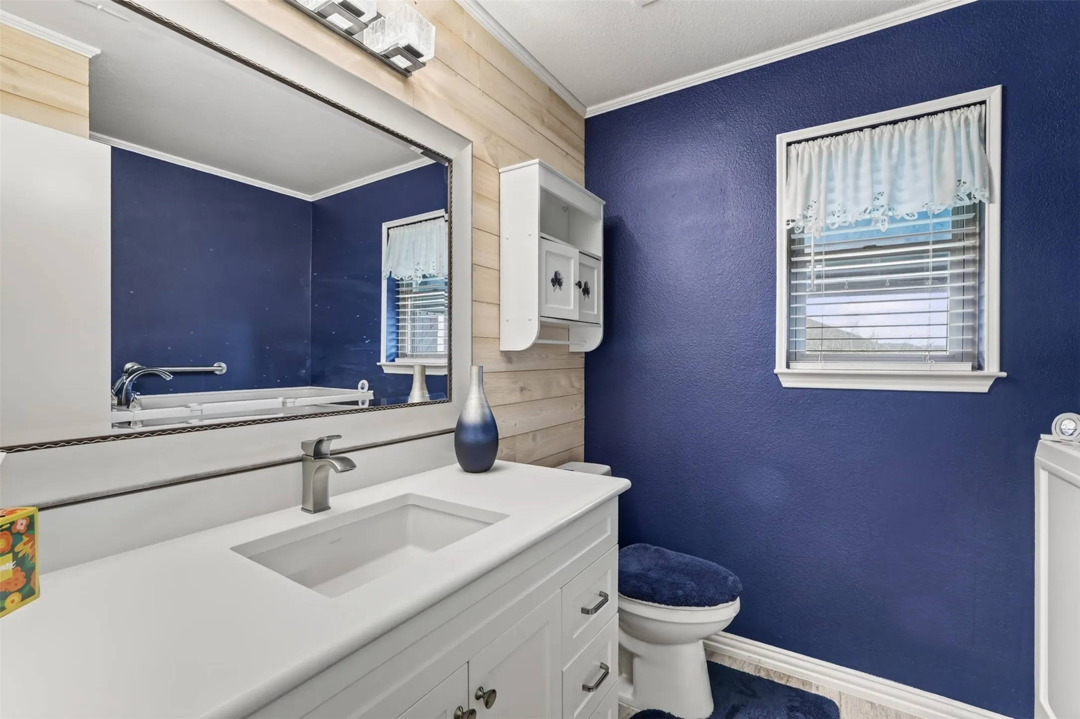 White vanity with integrated sink, brushed nickel faucet, and beadboard paneling in hall bath