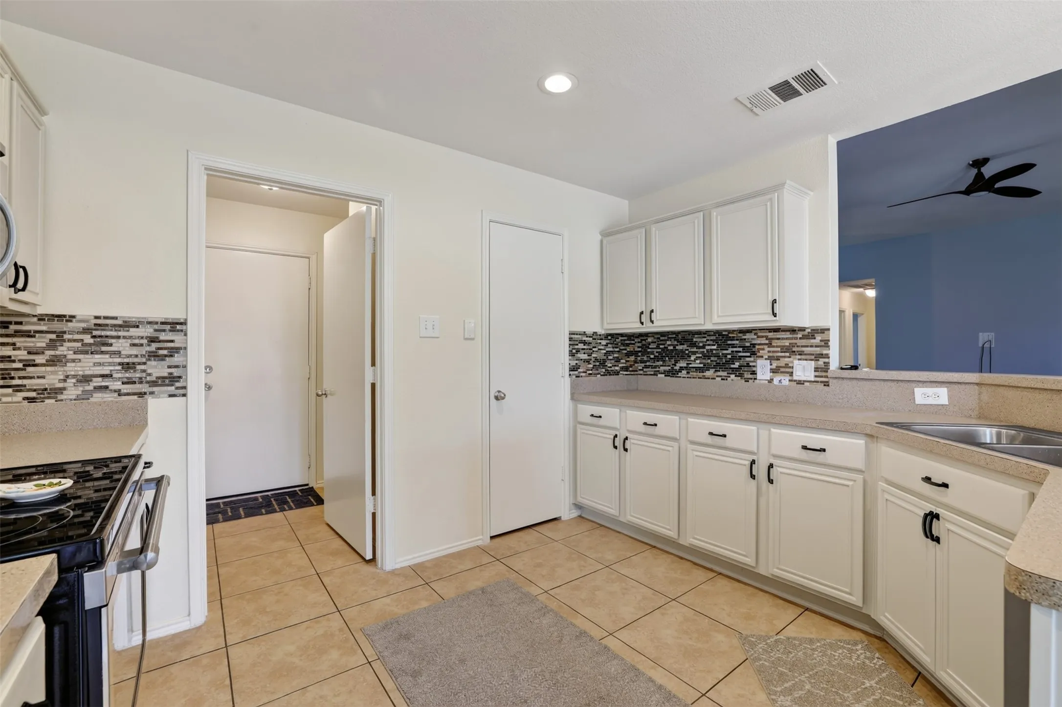 Kitchen featuring cream-colored cabinetry, tile backsplash, lots of countertop space, and a double basin sink