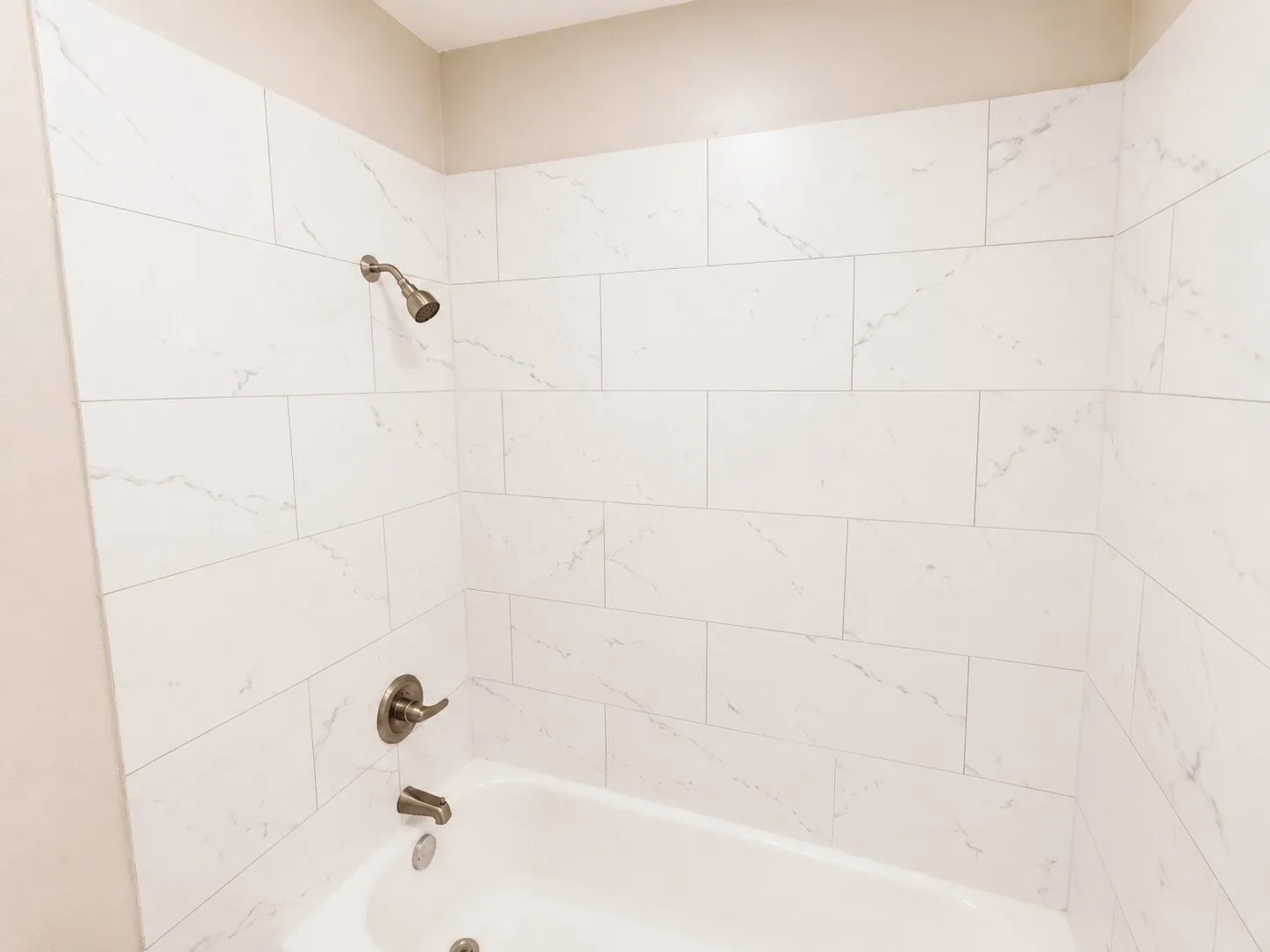 Bathtub with white subway-style tile surround, brushed nickel showerhead, and matching faucet with lever handle
