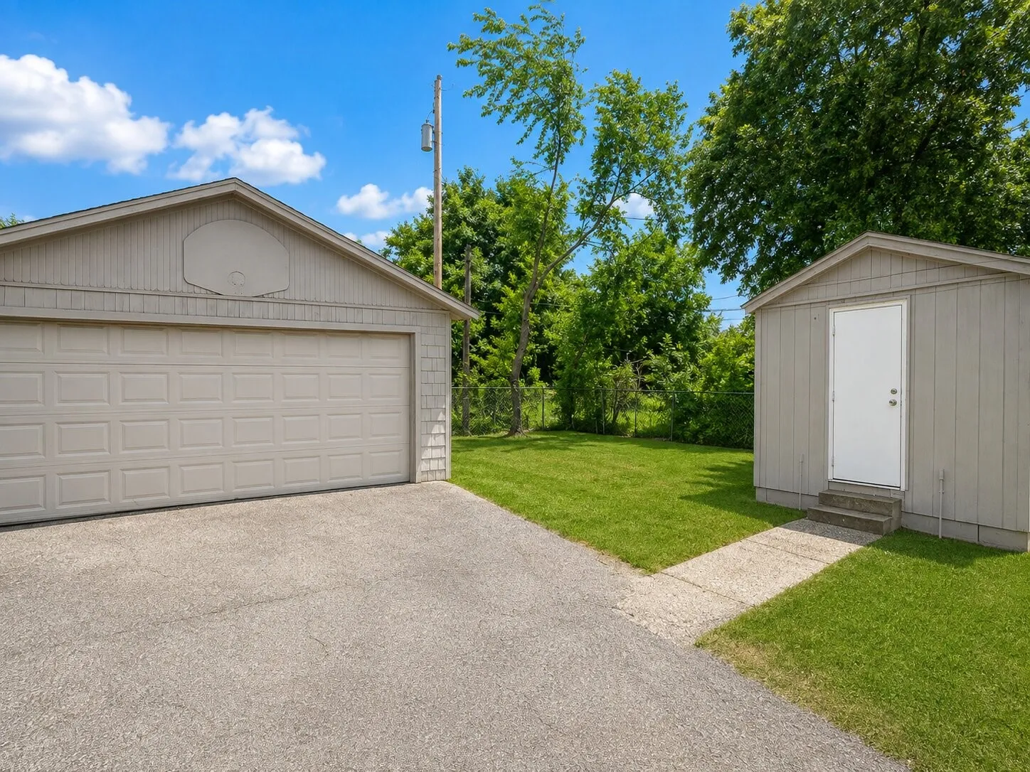 Detached two-car garage with a panel door, separate storage shed, and paved driveway