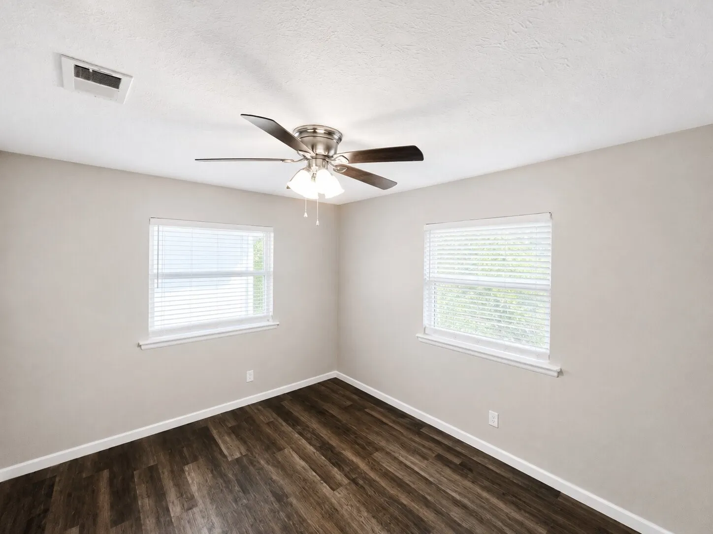 Wood-finish flooring, two windows with blinds, ceiling fan with integrated lighting, and neutral wall tones