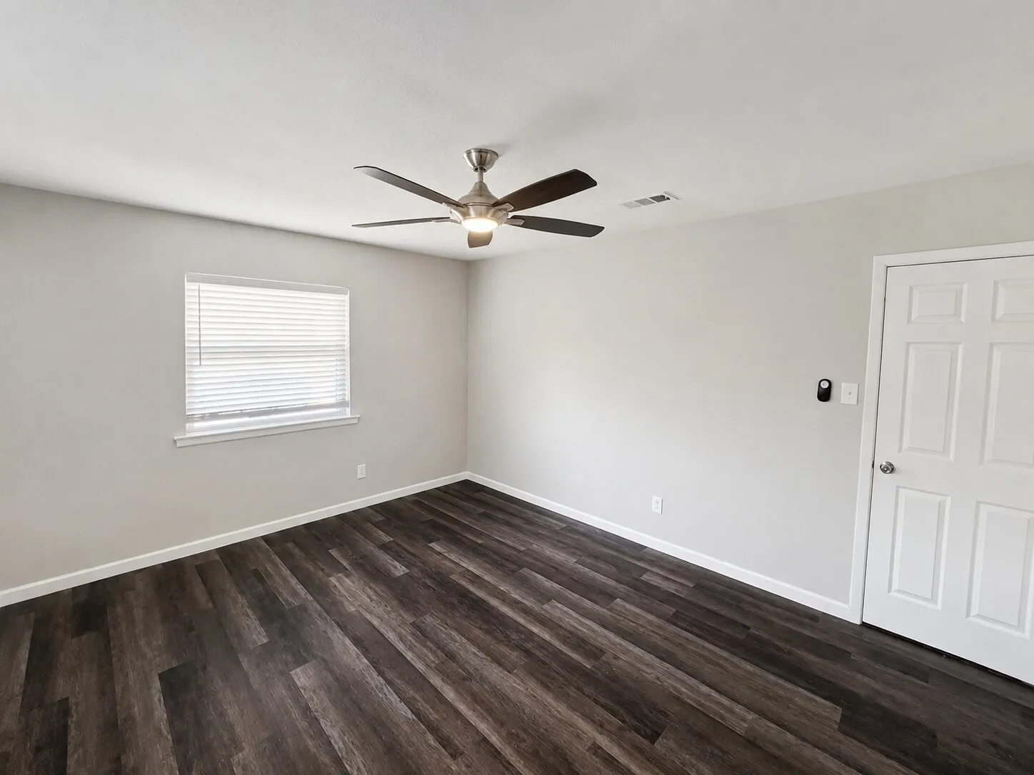 Wood-finish plank flooring, neutral wall paint, and a ceiling fan with integrated lighting