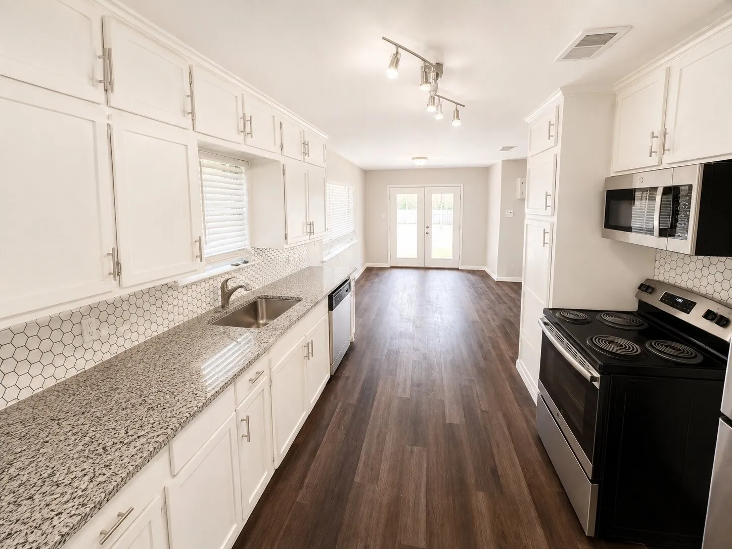 Galley kitchen featuring white cabinetry, granite countertops, a hexagonal tile backsplash, and wood-finish flooring