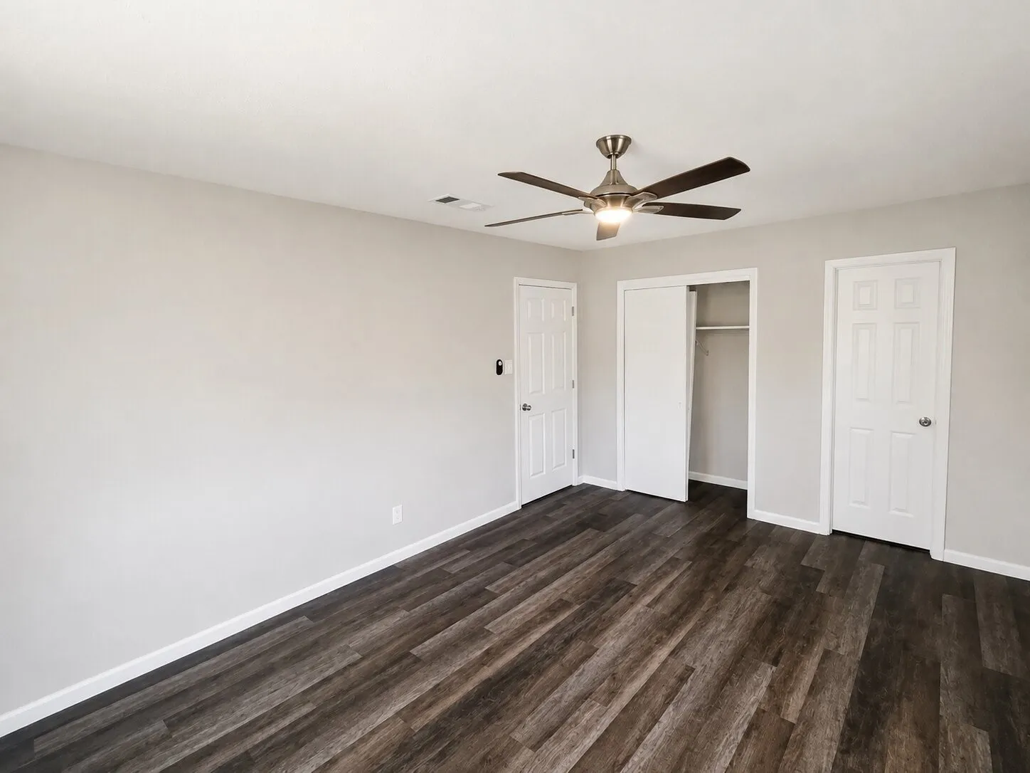 Wood-finish flooring, ceiling fan with integrated lighting, white panel doors, and a built-in closet with sliding doors
