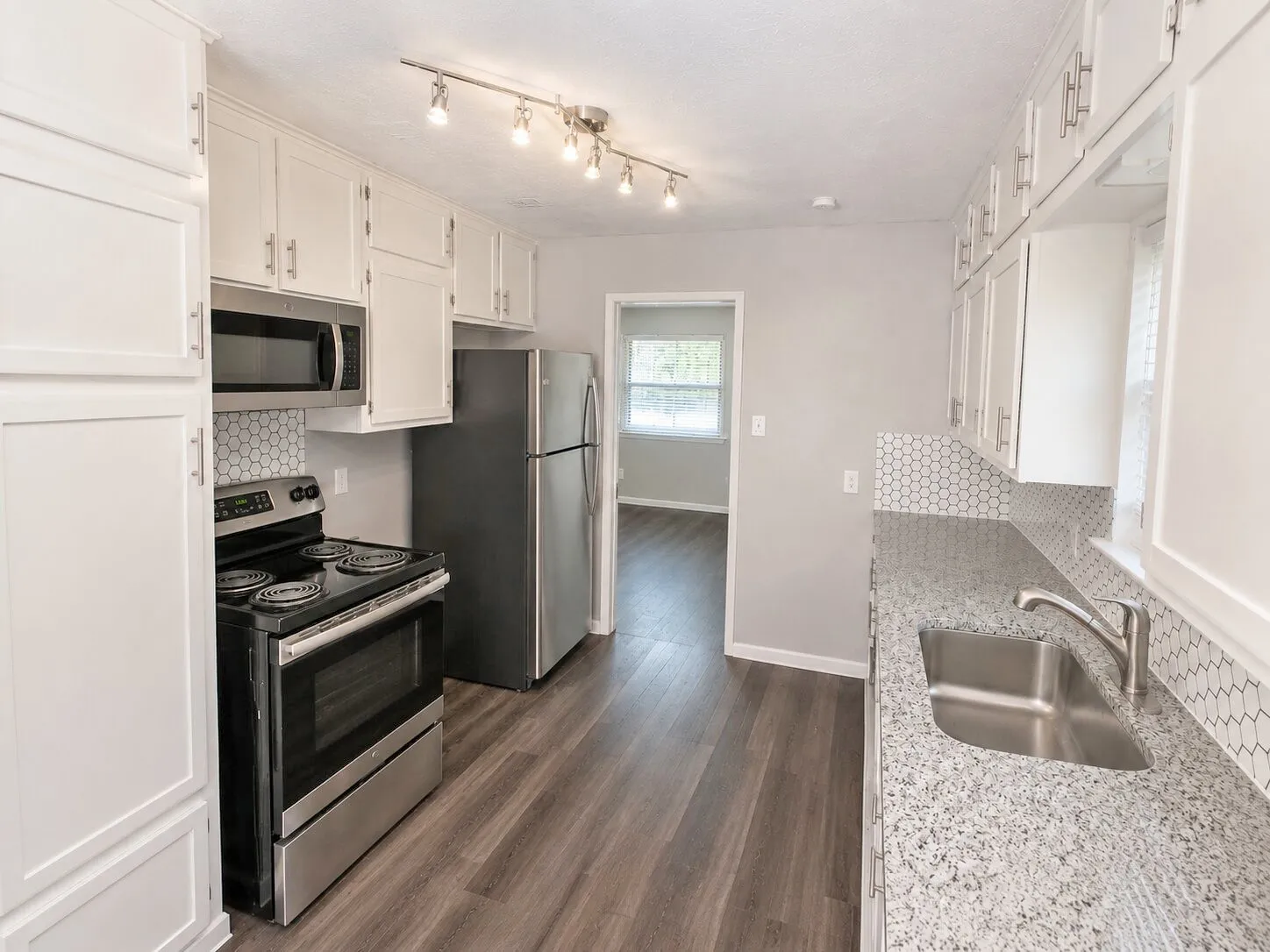 Kitchen featuring wood-finish flooring, white cabinetry, stainless steel appliances, a honeycomb tile backsplash, and granite-style countertops