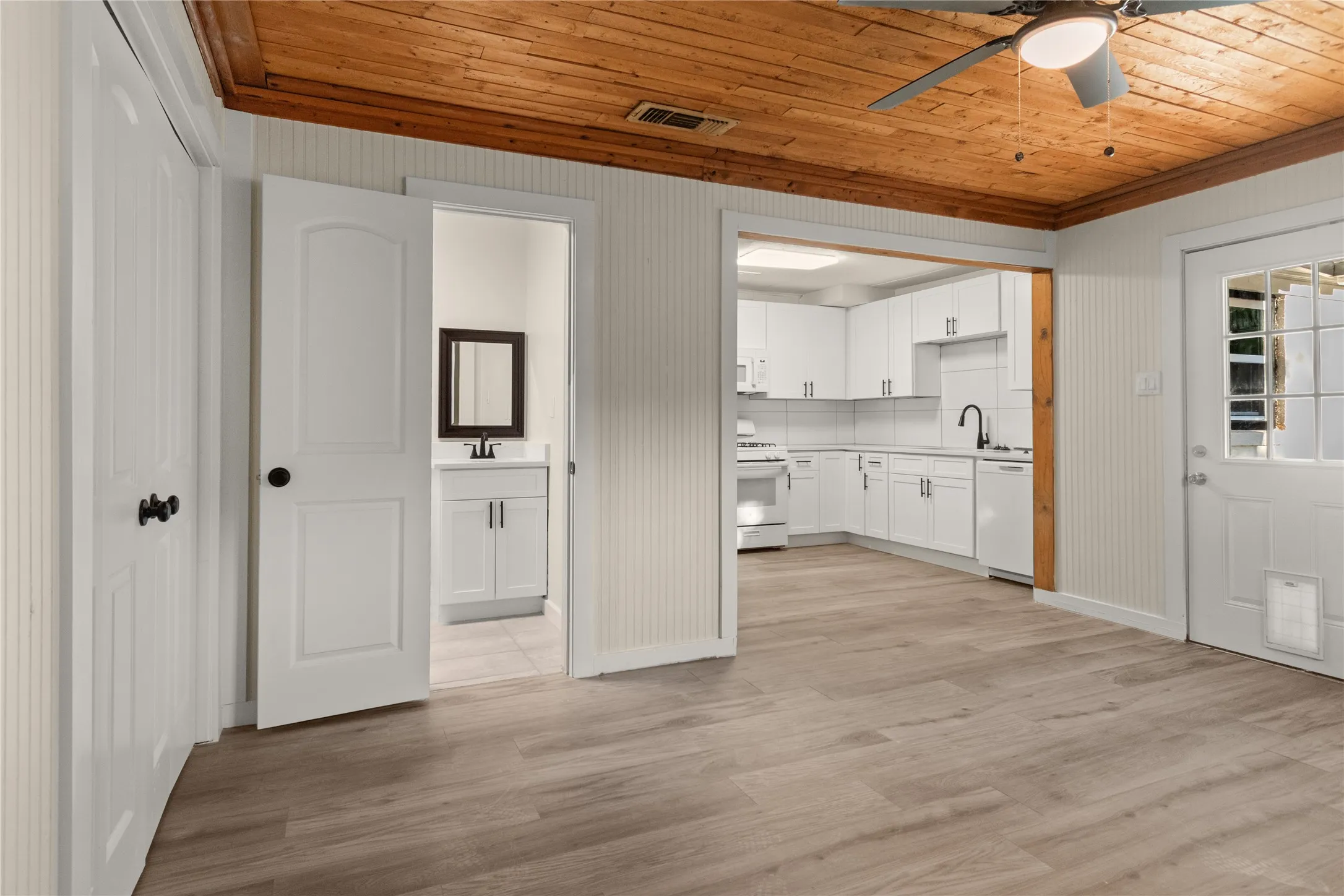3rd bedroom or flex space. LVP flooring, wood plank ceiling, closet, laundry room and full-bathroom. View into the kitchen.