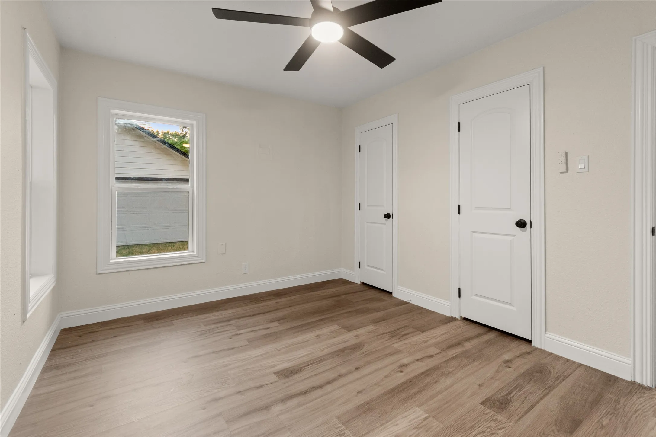 Bedroom #2 has a ceiling fan with black blades, two closets with built-in shelving, wood-finish flooring, white doors with black hardware, and three windows