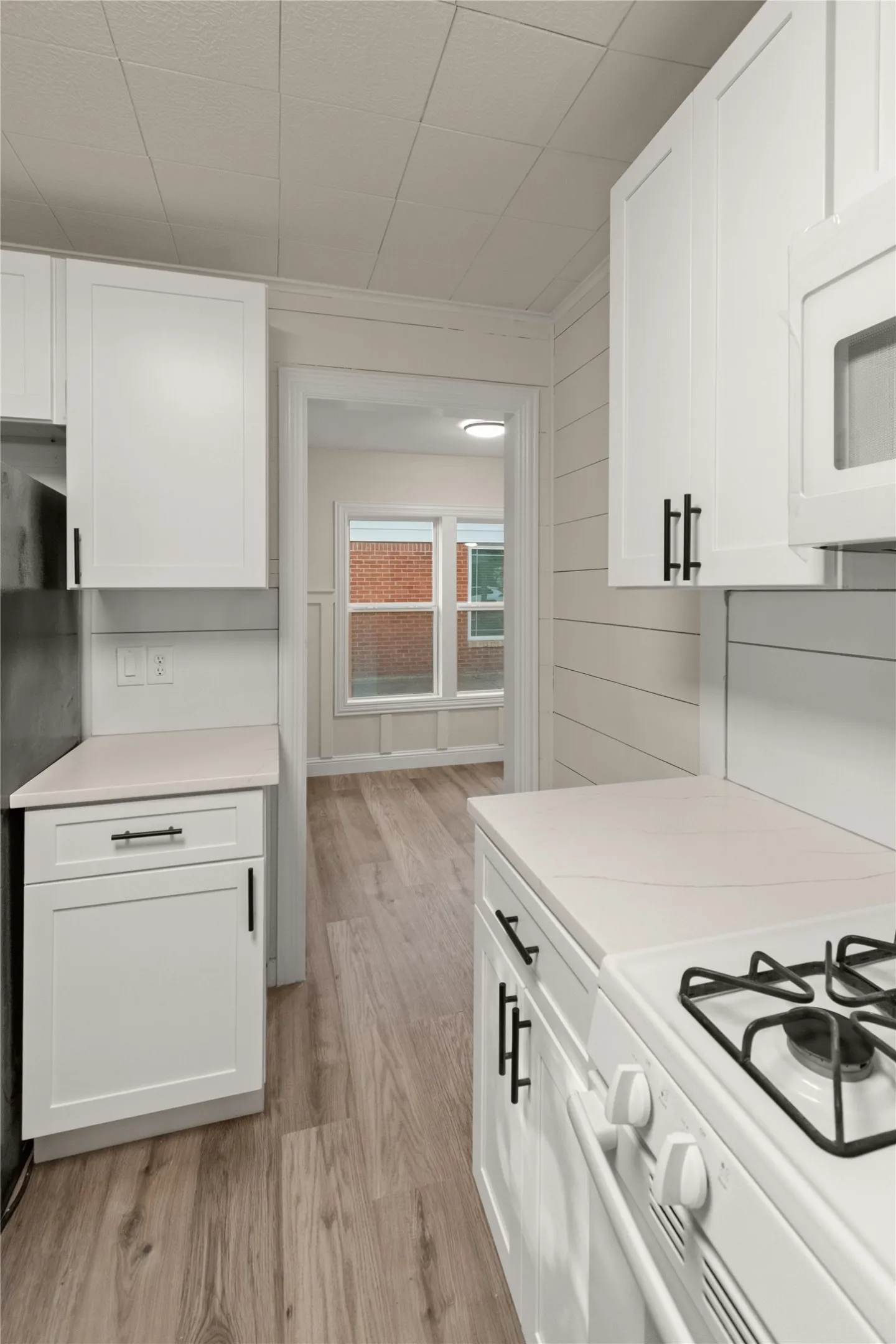 Kitchen with white shaker cabinetry, quartz countertops, white gas range, and wood-finish flooring. View from the kitchen into the dining room.