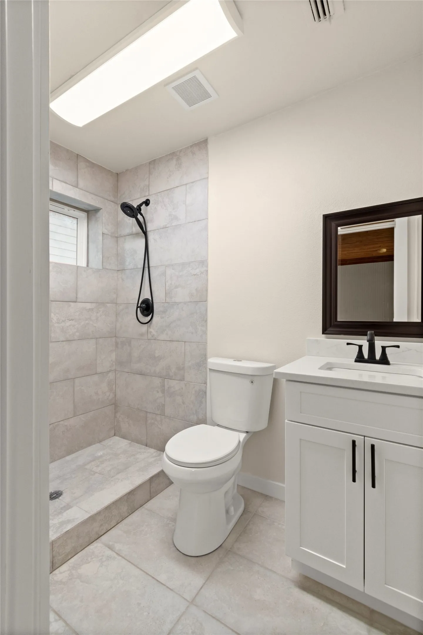 Rear 2nd full-bathroom. Tiled shower with matte black fixtures, white vanity with quartz countertop, dark framed mirror, and tiled flooring