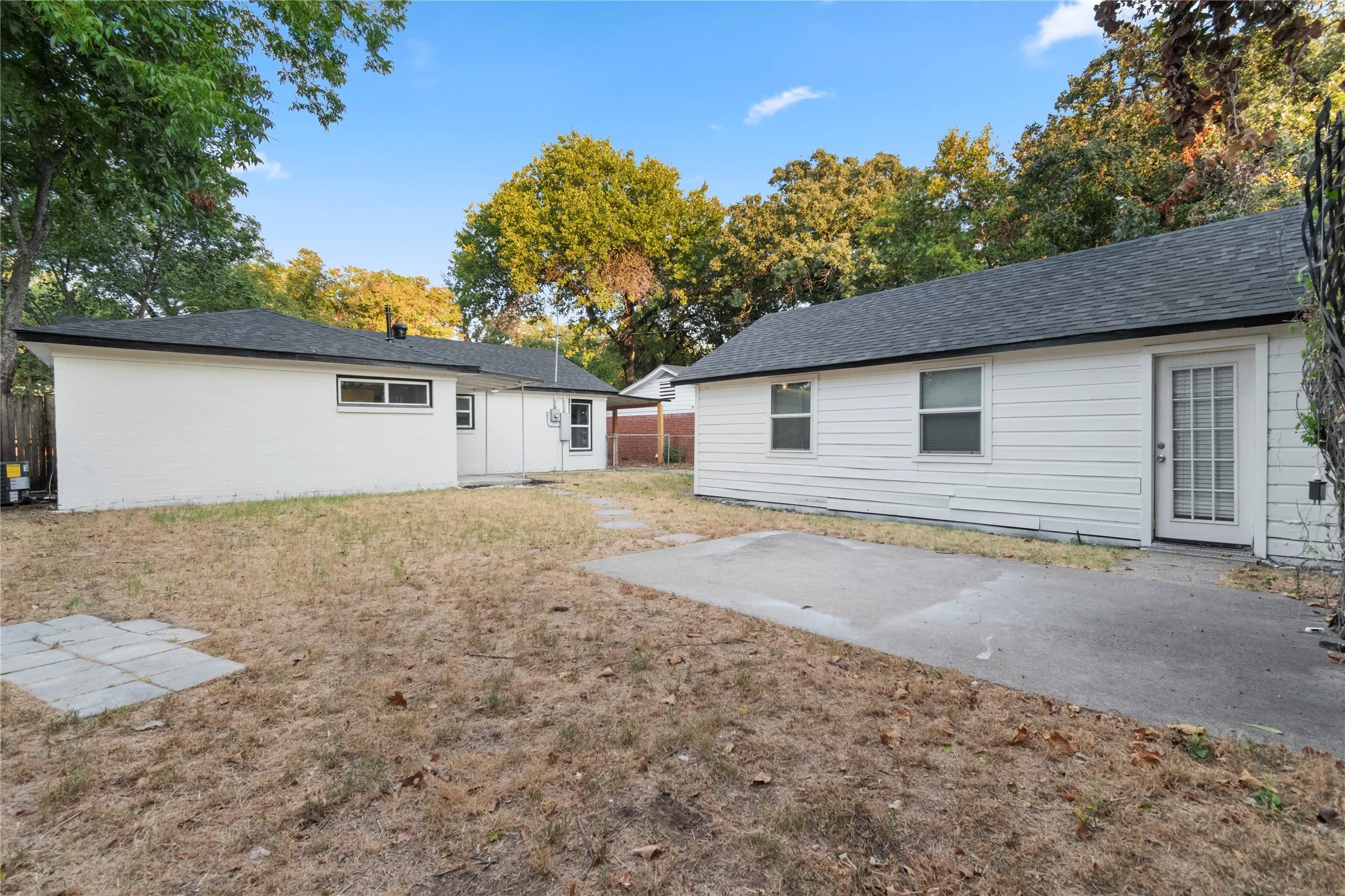 Backyard view of home and the 2-car garage featuring white siding, side door access and dark shingle roofs.