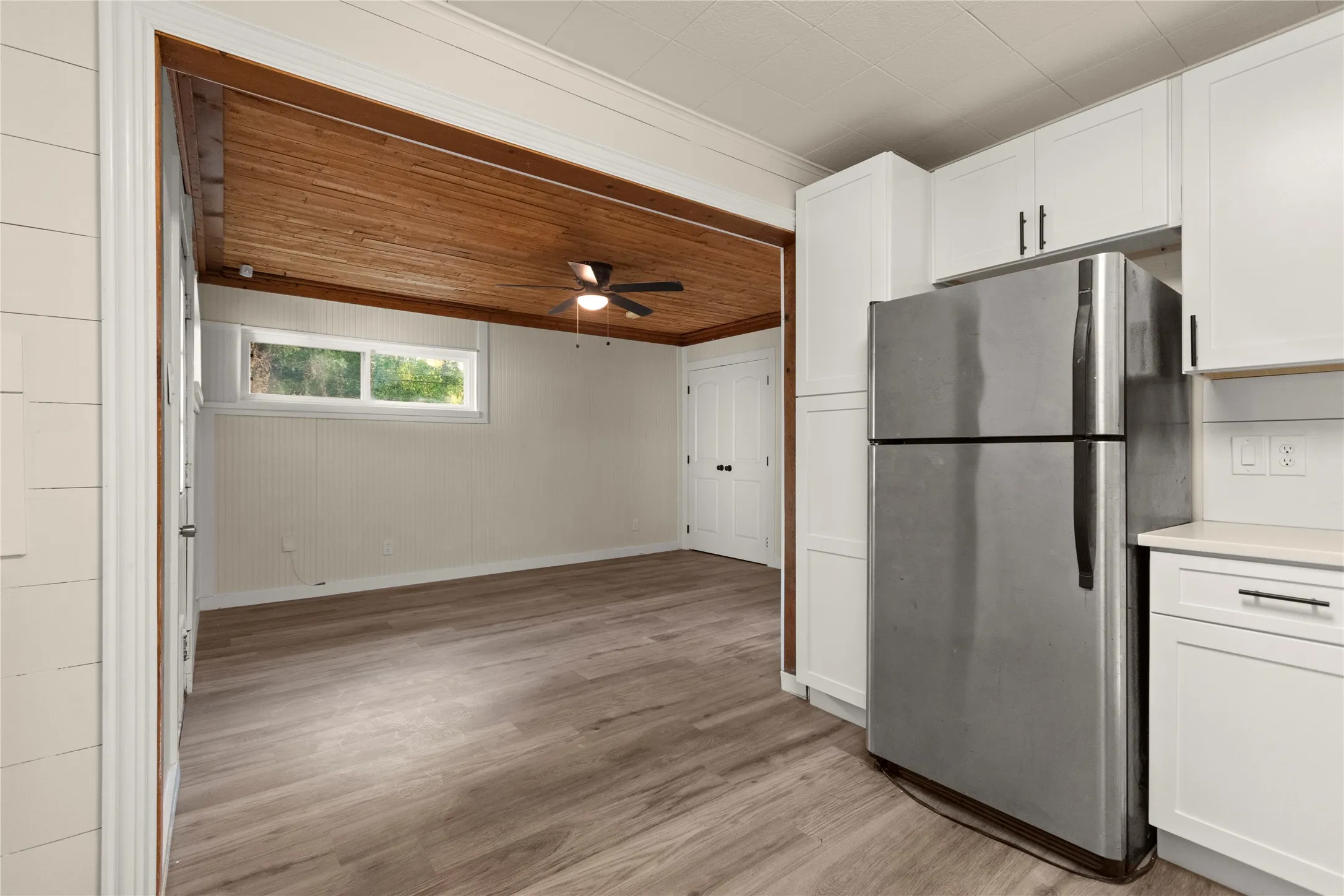 View from the kitchen to the wood plank ceiling rear living area or bedroom. White cabinetry with dark hardware, quartz countertop and wood-finish flooring,