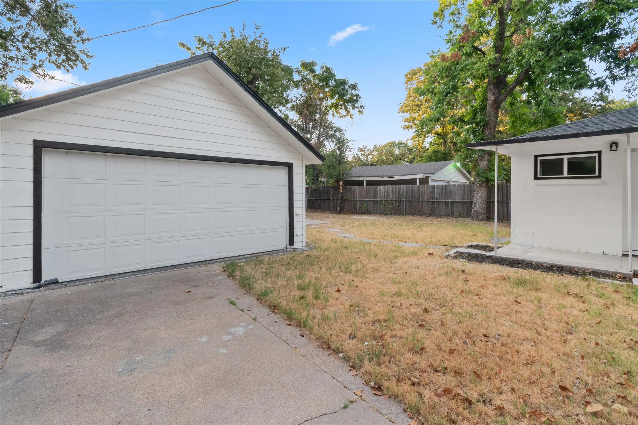 Detached 2-car garage with panel door in the backyard white painted exterior, covered porch, and concrete patio