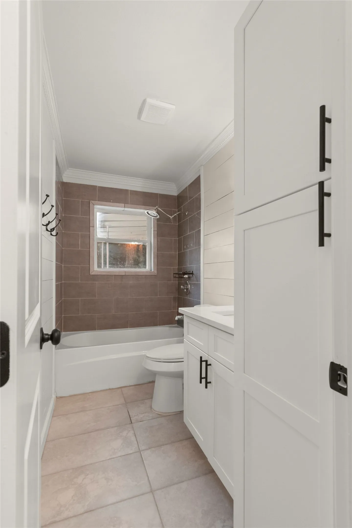 Hallway full-bathroom. White shaker-style cabinetry with matte black hardware, quartz countertop, and tiled flooring.