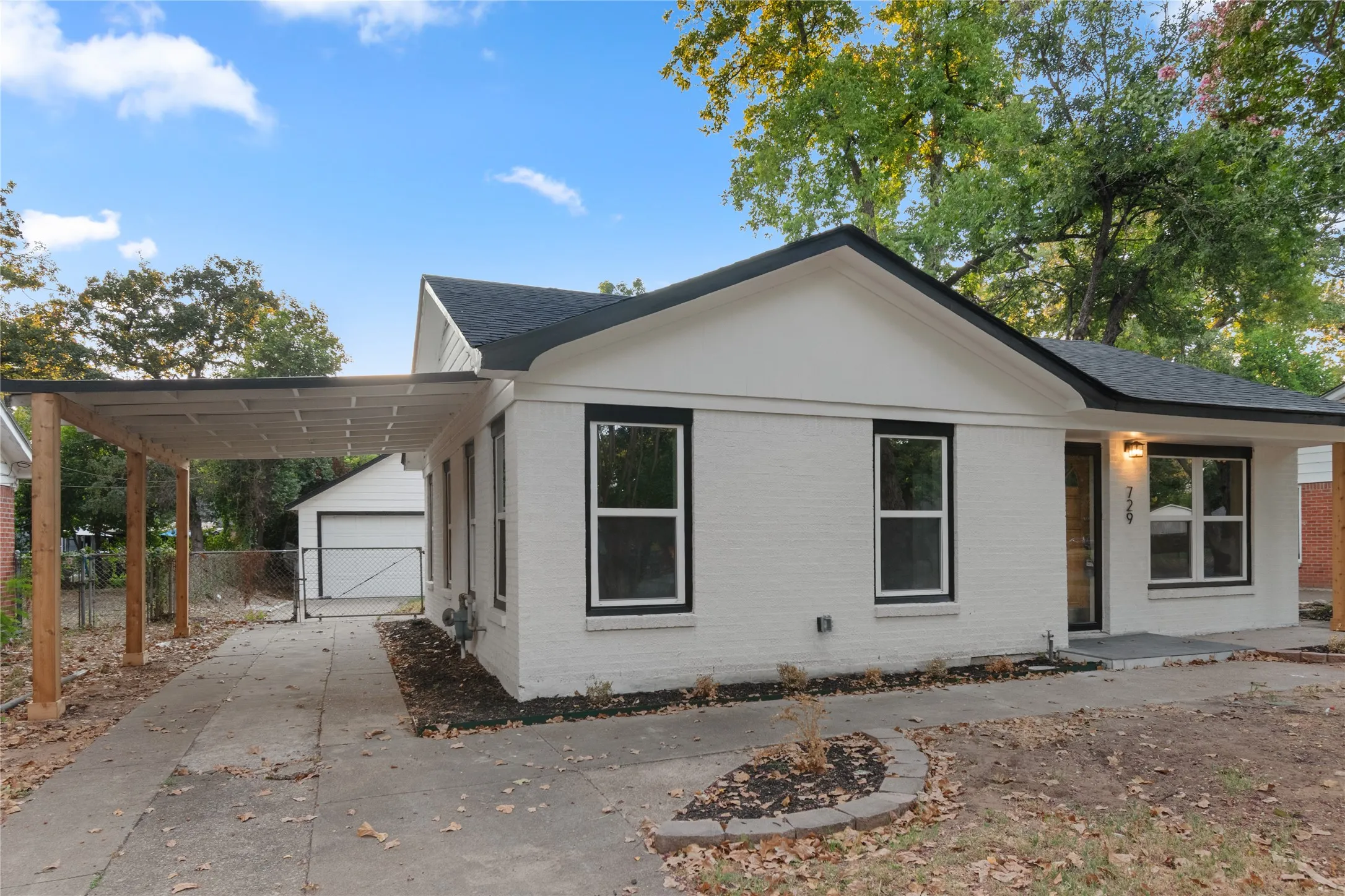 White brick exterior with black framed windows, a black roof, and an attached carport. 2-car garage in the backyard.
