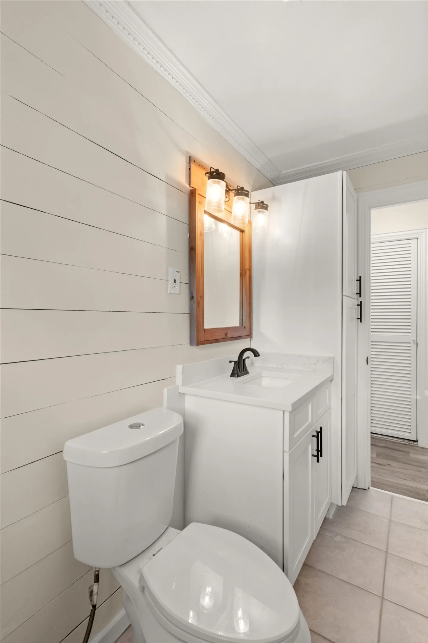 Hallway full-bathroom. Shiplap accent wall with crown molding, white shaker cabinet vanity with black hardware, quartz countertop with integrated sink, and tile flooring