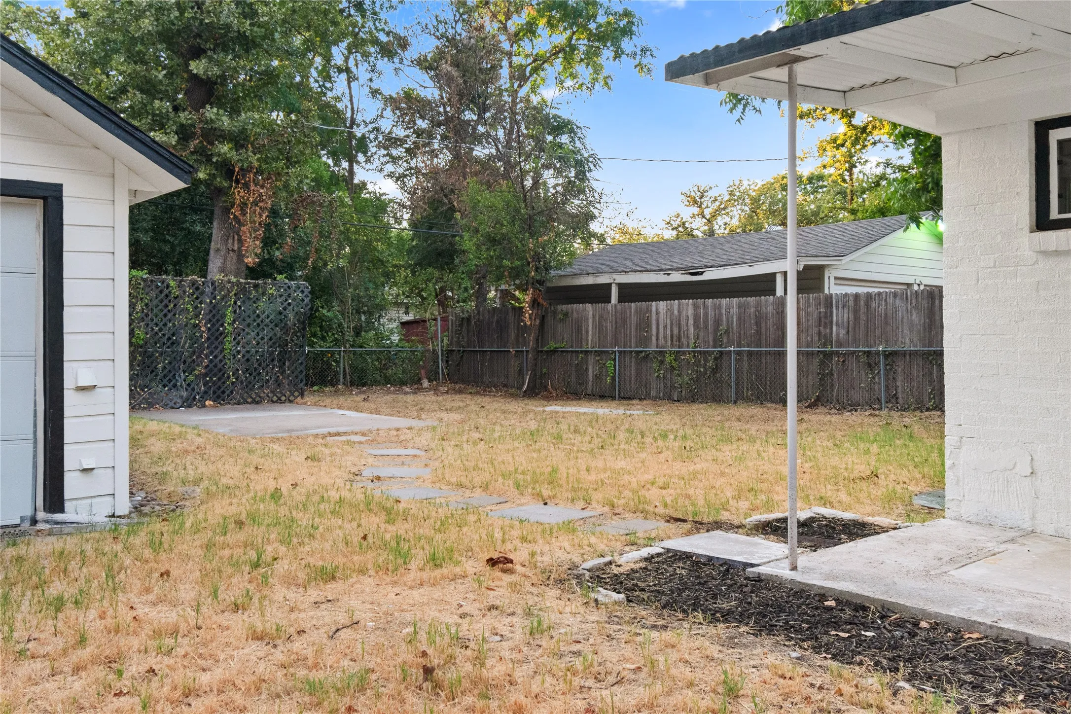 Expansive backyard featuring a concrete patio, stepping stones, 2-car garage and wood fencing