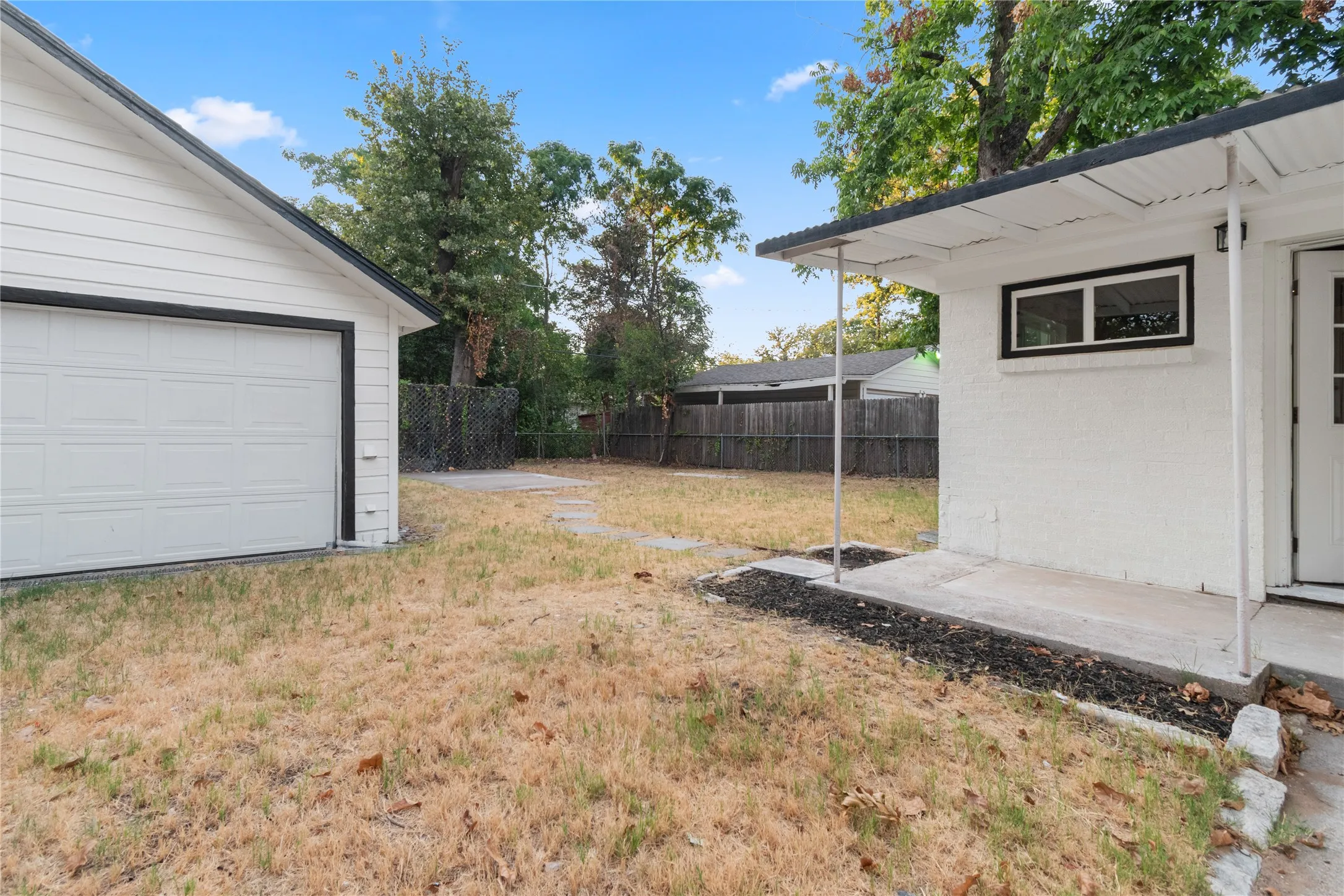 Detached 2-car garage with panel door, white painted brick exterior, covered porch, and concrete patio