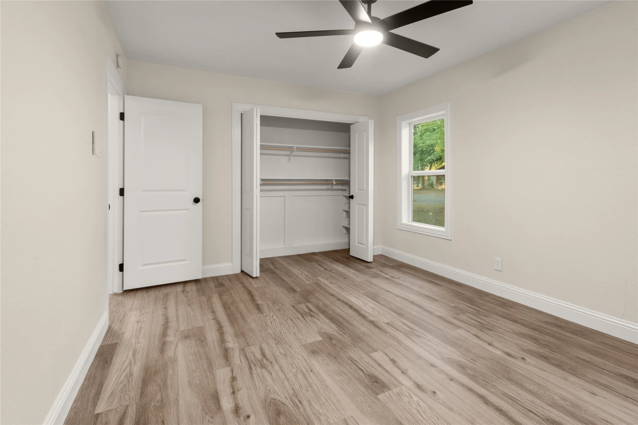 Bedroom #1 with wood-finish flooring, an integrated ceiling fan with lighting, large built-in closet with shelving, and three bright windows