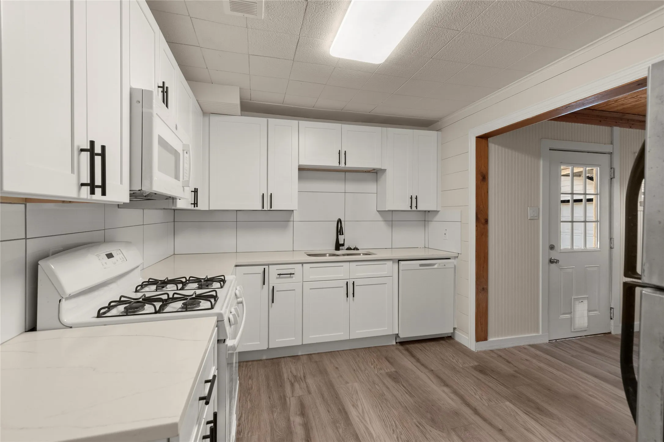 White cabinetry with matte black hardware, white tile backsplash, quartz countertops, wood-finish flooring, and a white gas range