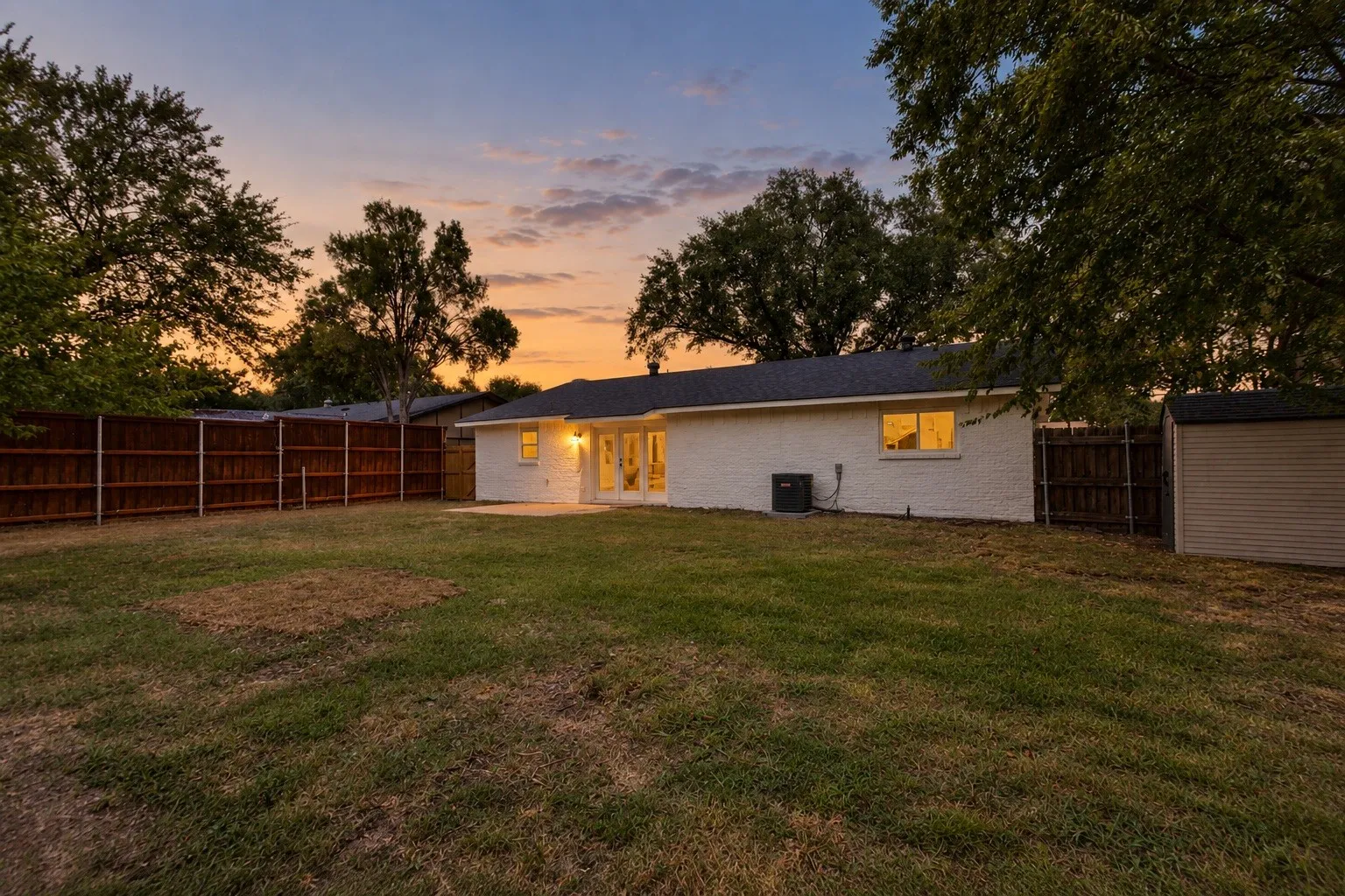 Expansive backyard featuring a manicured lawn, a privacy fence, and an exterior storage shed