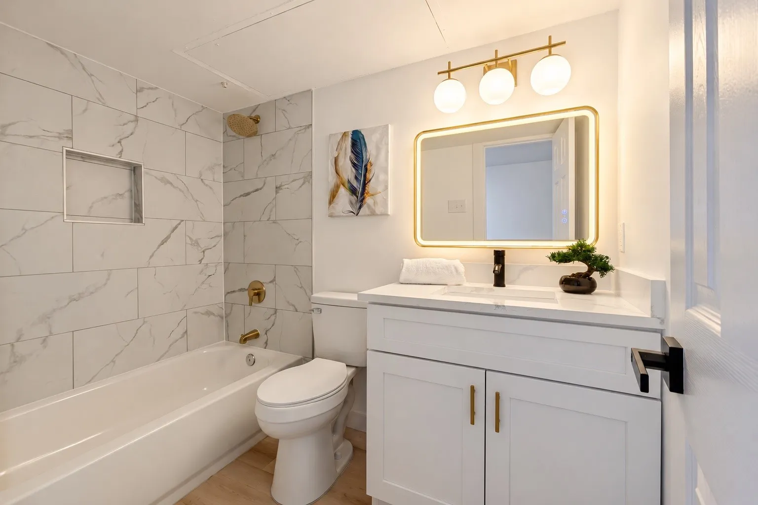 Bathroom featuring a built-in tub with gold-tone fixtures, white marble-style wall tiling, and a built-in shower niche