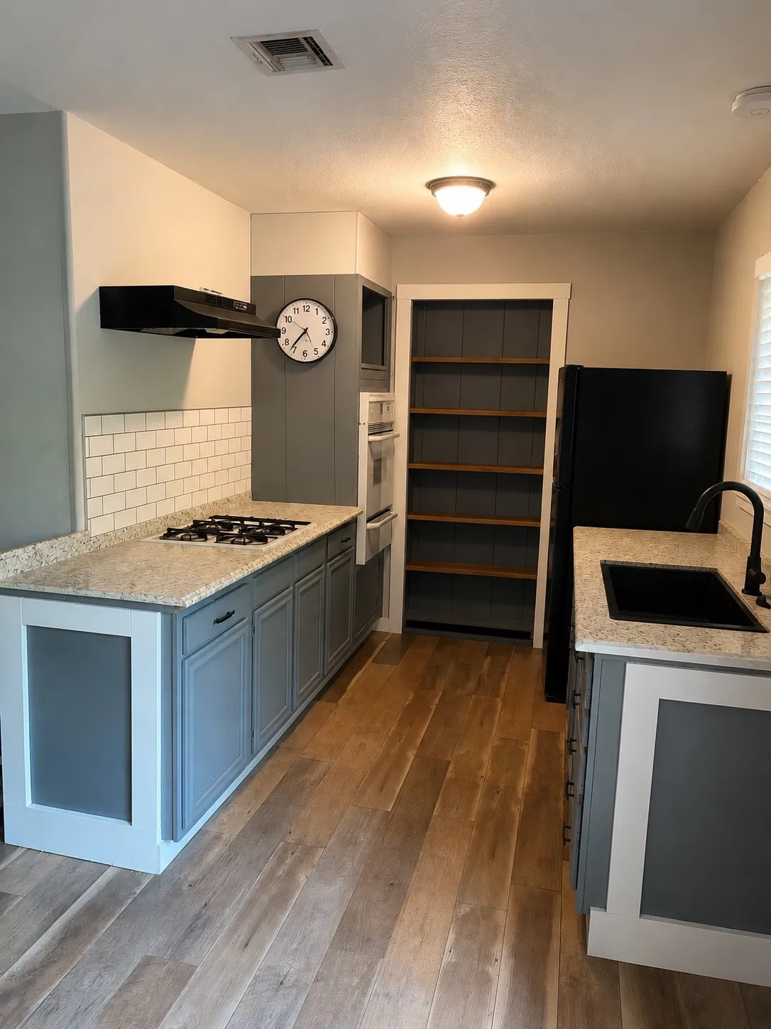 Wood-finish flooring, light-toned countertops, white subway tile backsplash, built-in shelving, and recessed lighting