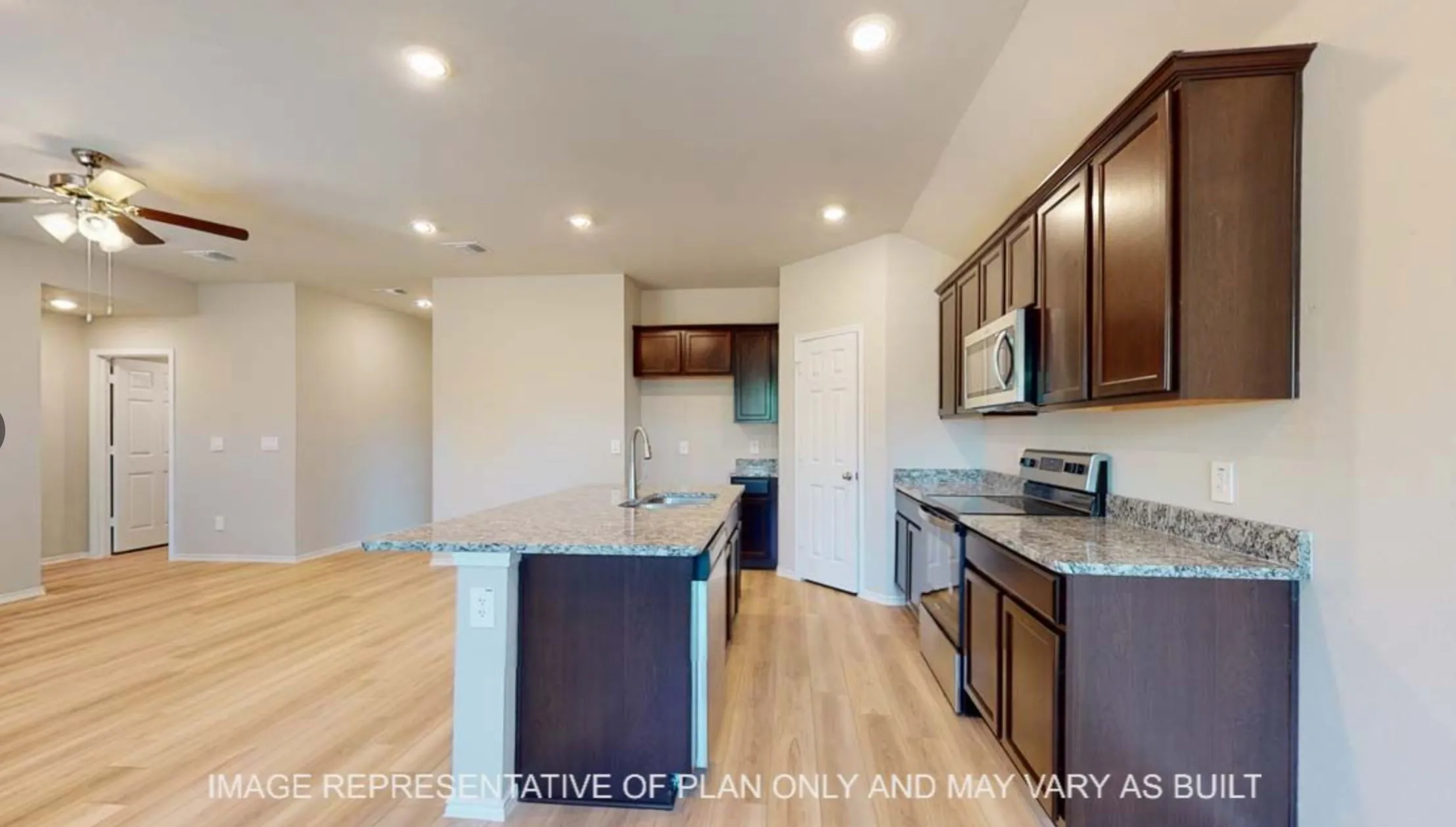 Spacious kitchen featuring dark wood cabinetry, light-toned countertops, stainless steel appliances, a center island with sink, and wood-finish flooring