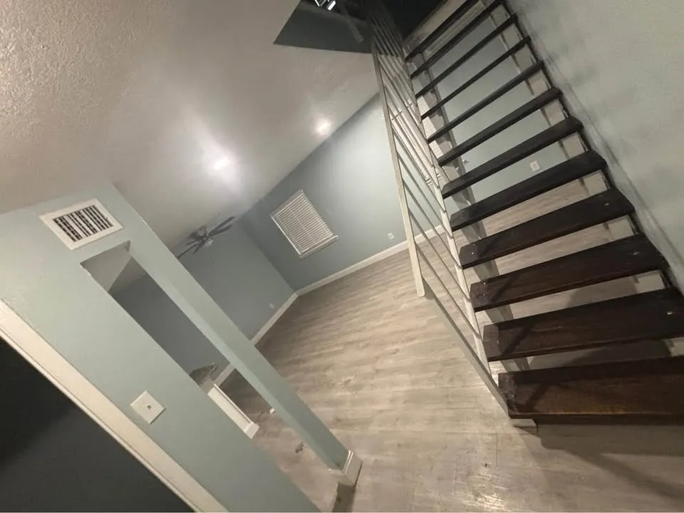 Wood-finish flooring, dark wood stairs, white railing, ceiling fan, and blinds