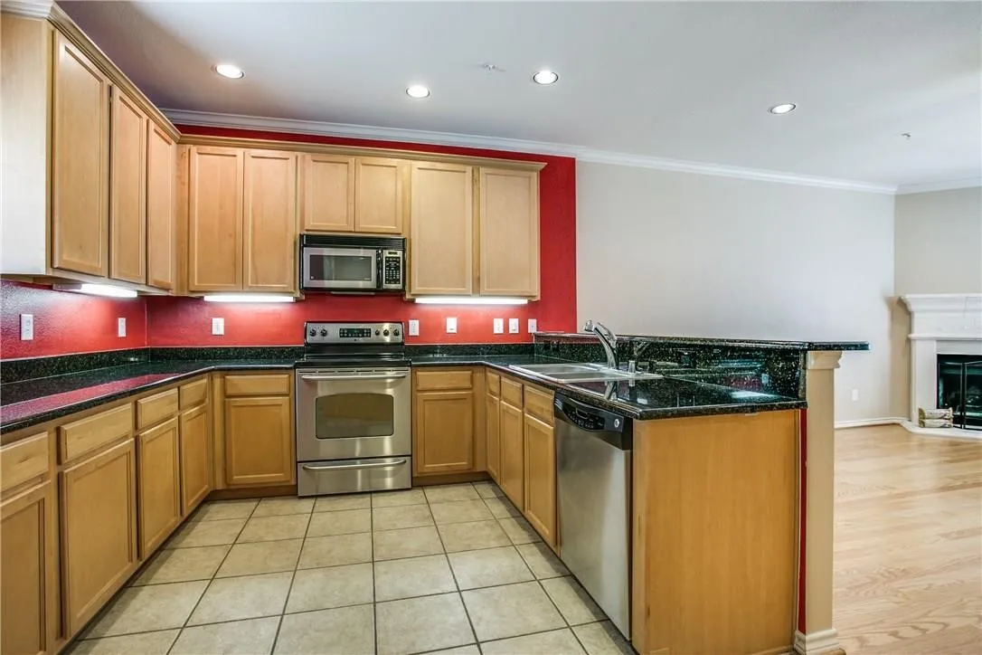 U-shaped kitchen featuring wood-finish cabinetry, dark countertops, stainless steel appliances, and tile flooring