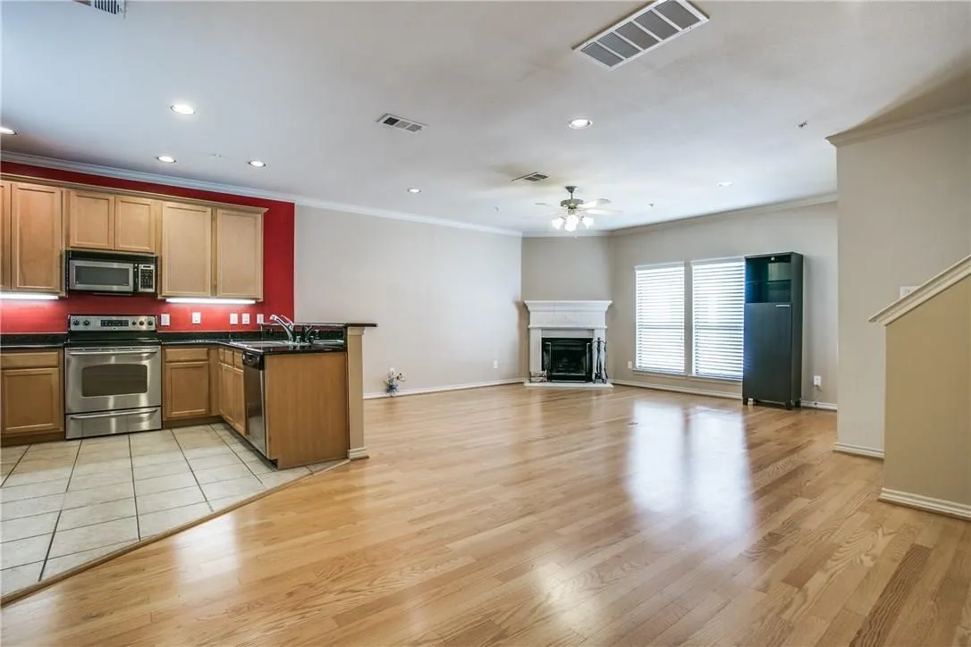 Open-concept living area with wood-finish flooring, a kitchen featuring stainless steel appliances, and a fireplace with a detailed mantel