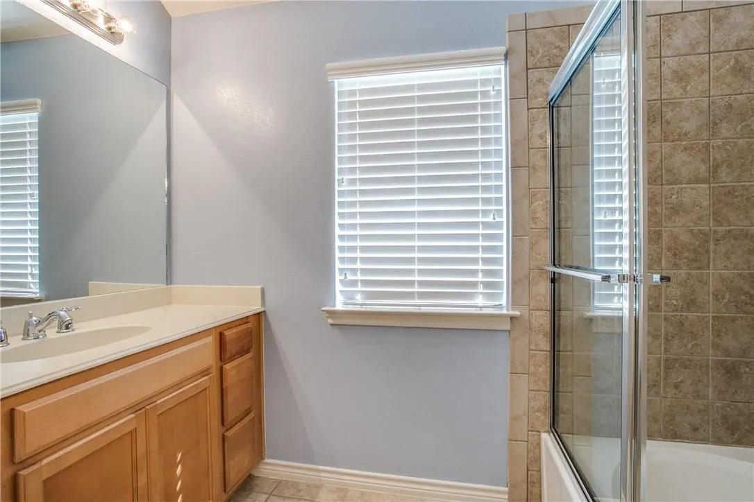 Bathroom featuring a vanity with an integrated sink, wood-finish cabinetry, and a tile-surround shower with a glass enclosure