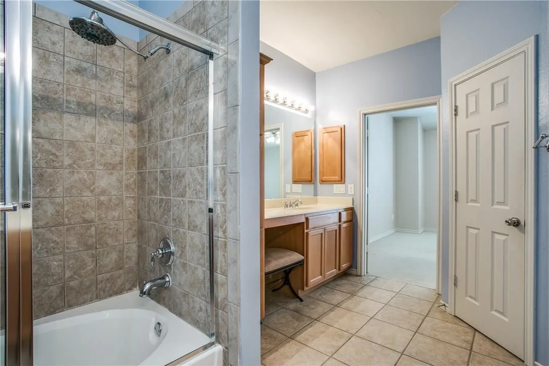 Tub and shower combination with tiled surround, glass enclosure, wood-finish vanity with countertop, and tile flooring