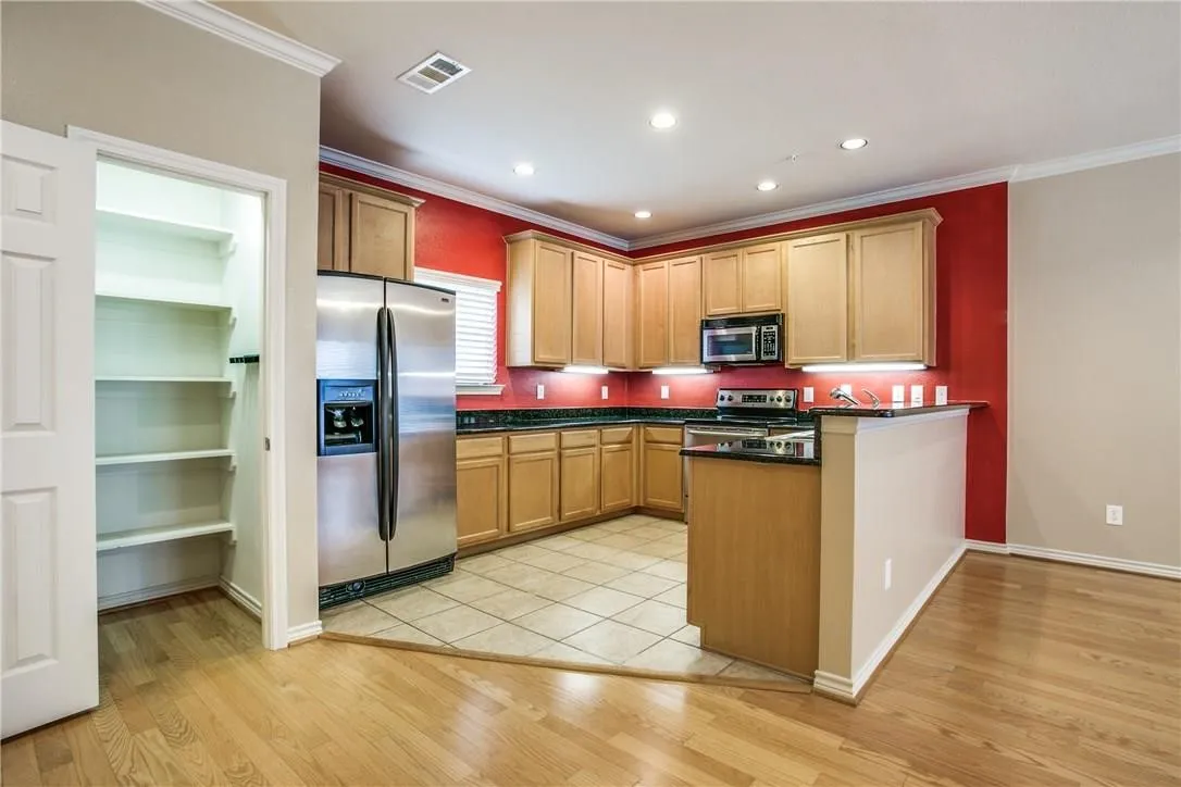 Kitchen featuring wood cabinetry, stainless steel appliances, dark countertops, and tile flooring