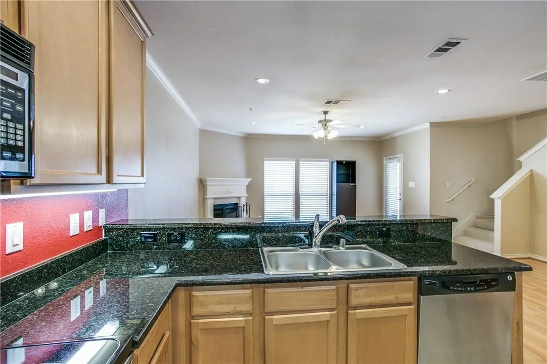 Kitchen with dark granite countertops, light wood cabinetry, and stainless steel appliances