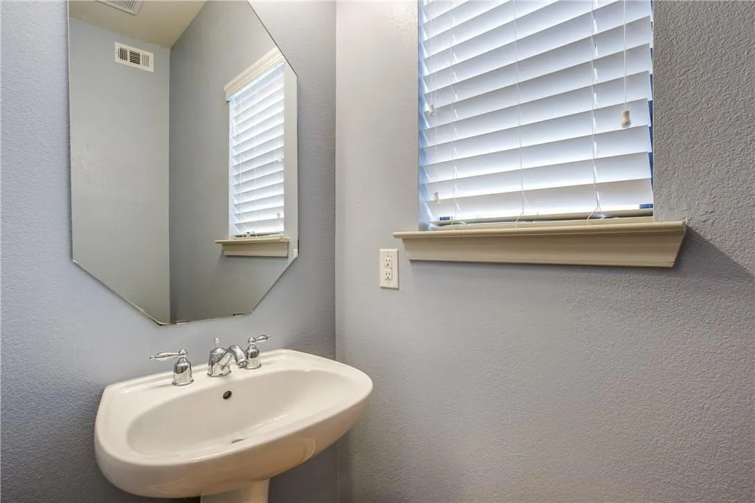 Pedestal sink with chrome fixtures, an octagonal mirror, and a window with blinds