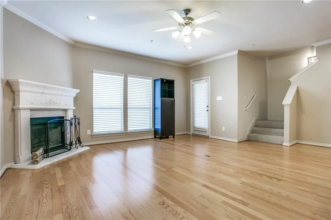 Hardwood flooring, fireplace with a stone mantel, ceiling fan with integrated lighting, recessed lighting, and a staircase with carpeted treads