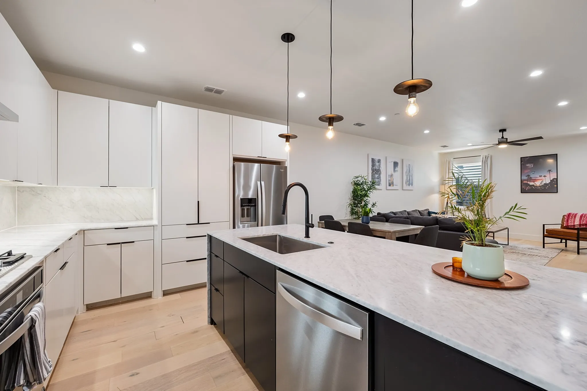 Modern kitchen featuring a large island with a stainless steel sink, stainless steel appliances, white flat-panel cabinetry, and light wood-finish flooring