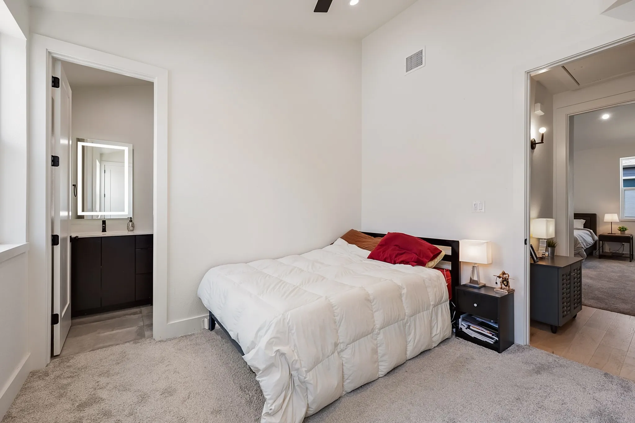 Carpeted room with a contemporary bed frame, a vanity with a rectangular basin, and an illuminated mirror