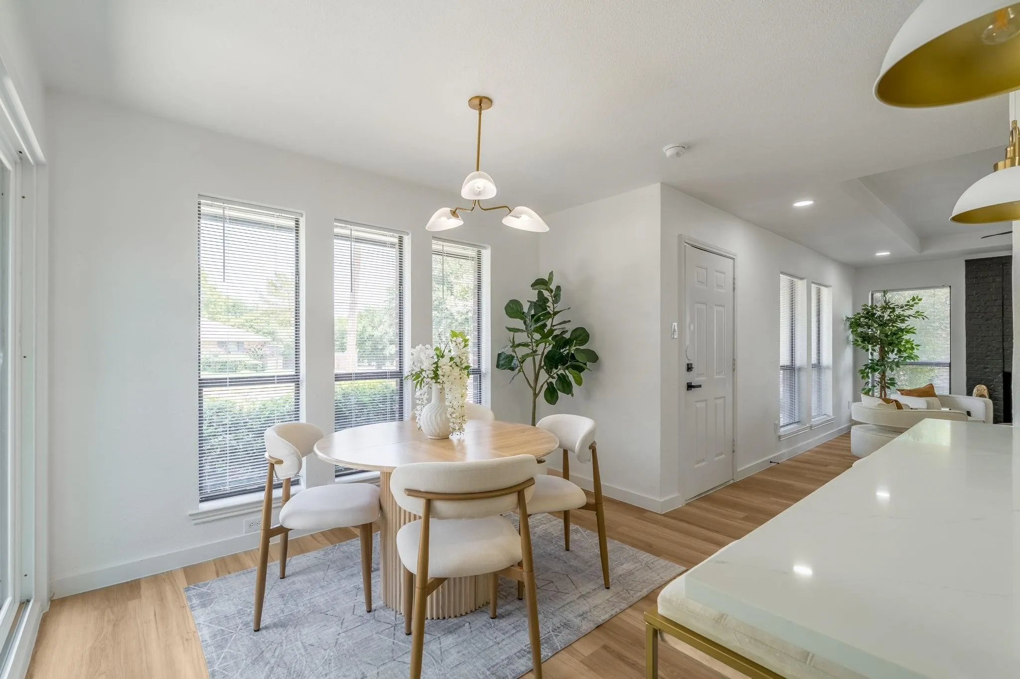 Wood-finish flooring, multiple windows with blinds, a modern ceiling light fixture, and a built-in kitchen island with a light-toned countertop
