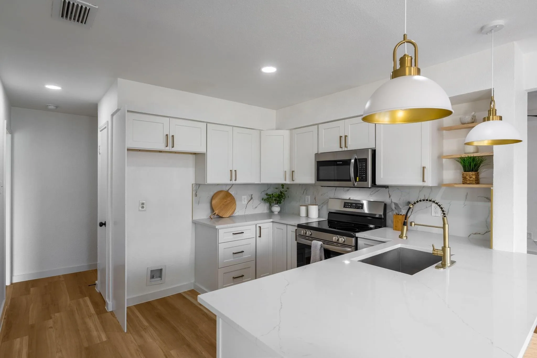 Contemporary kitchen featuring white cabinetry, stainless steel appliances, a white quartz island, a gold-tone faucet, and wood-finish flooring