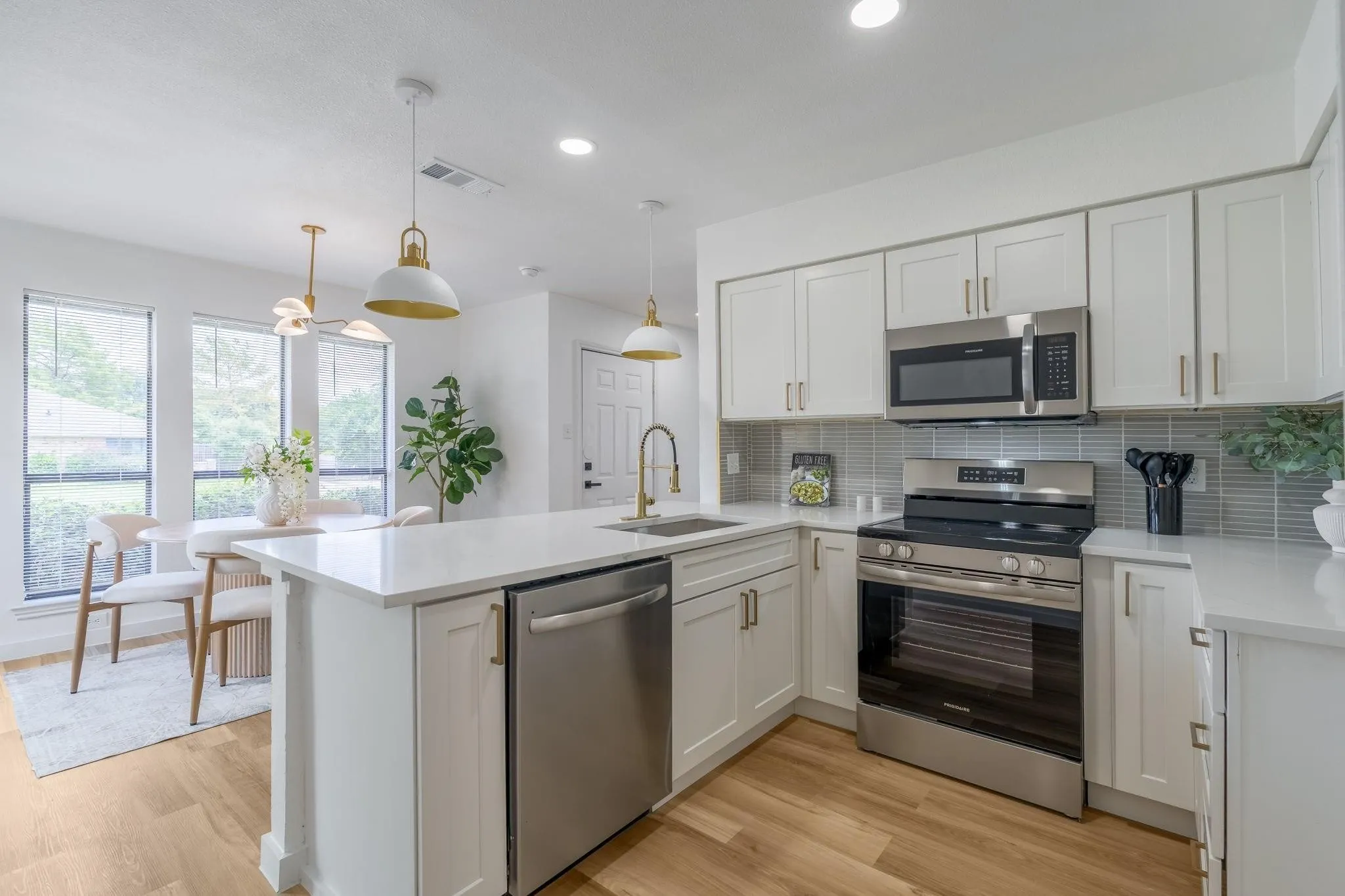 Kitchen featuring white shaker cabinetry, stainless steel appliances, light-toned wood-finish flooring, white countertops, and a tile backsplash