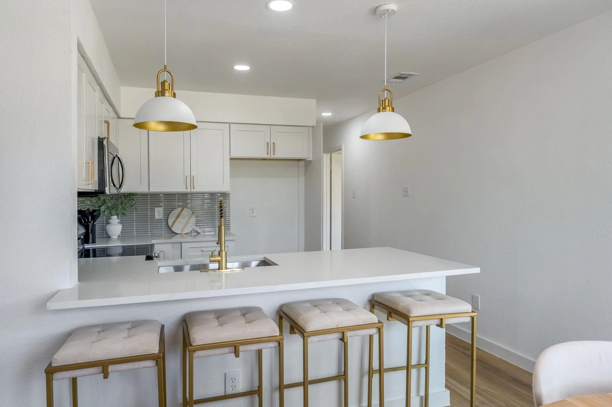 Kitchen featuring a white countertop island, pendant lighting, white cabinetry, a stainless steel microwave, and a tile backsplash