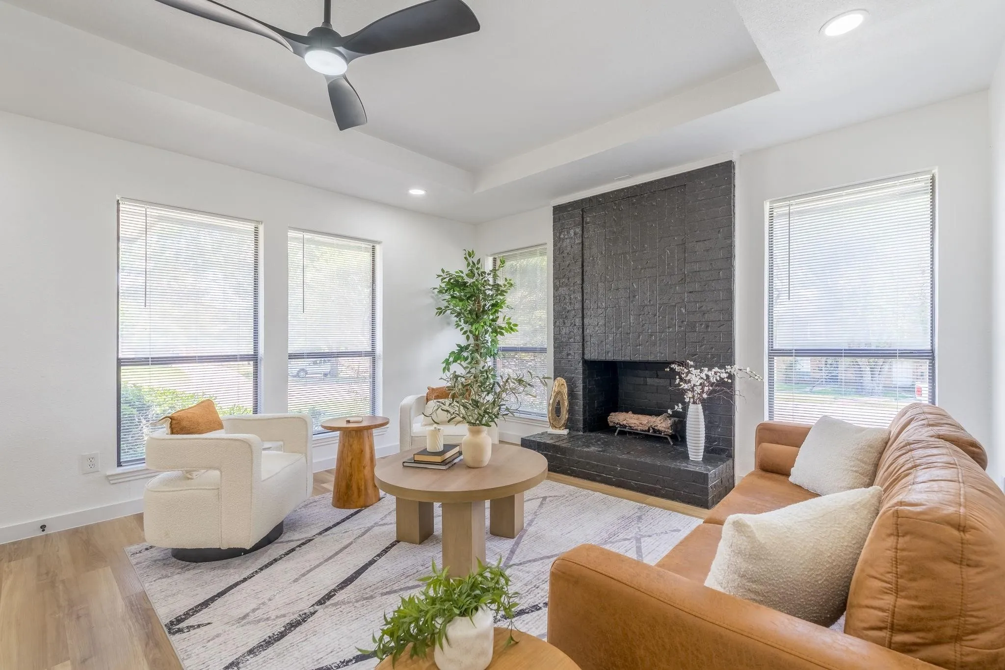 Tray ceiling with recessed lighting, black brick fireplace, wood-finish flooring, and large windows with blinds