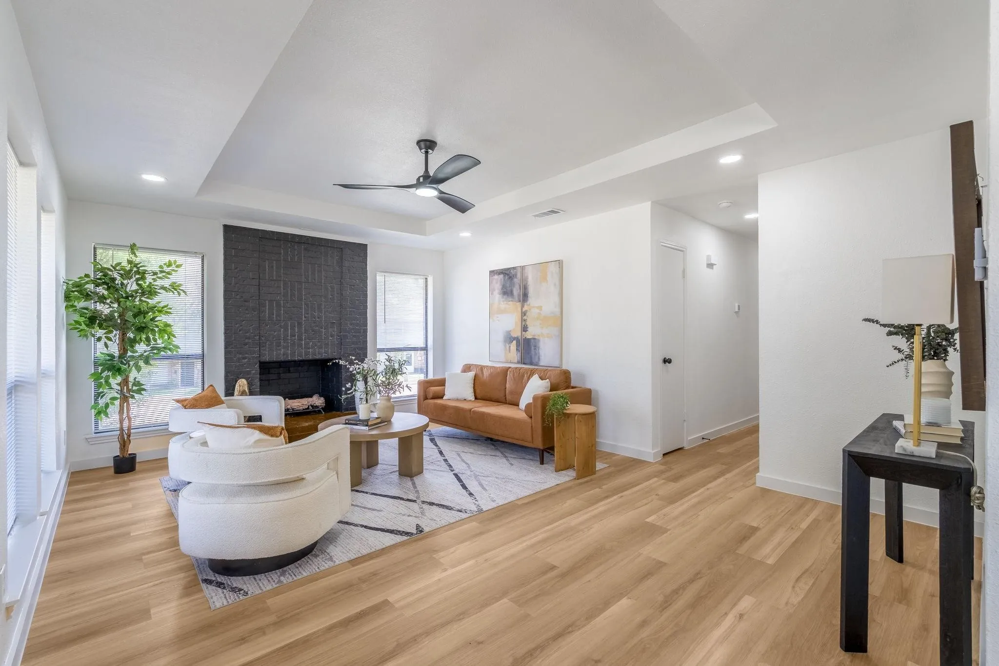 Spacious living area featuring wood-finish flooring, a tray ceiling with a ceiling fan, and a textured black fireplace surround