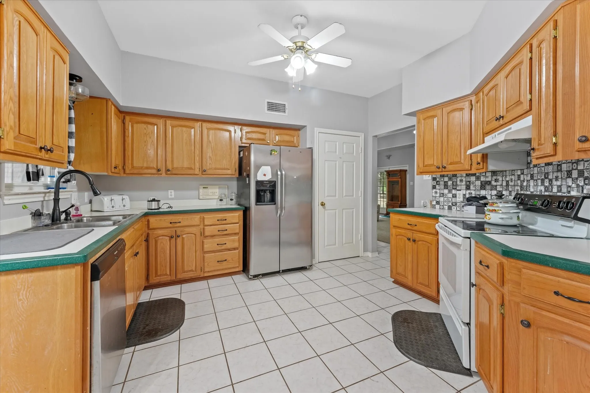 Kitchen featuring wood cabinetry, tile flooring, stainless steel refrigerator, and a ceiling fan