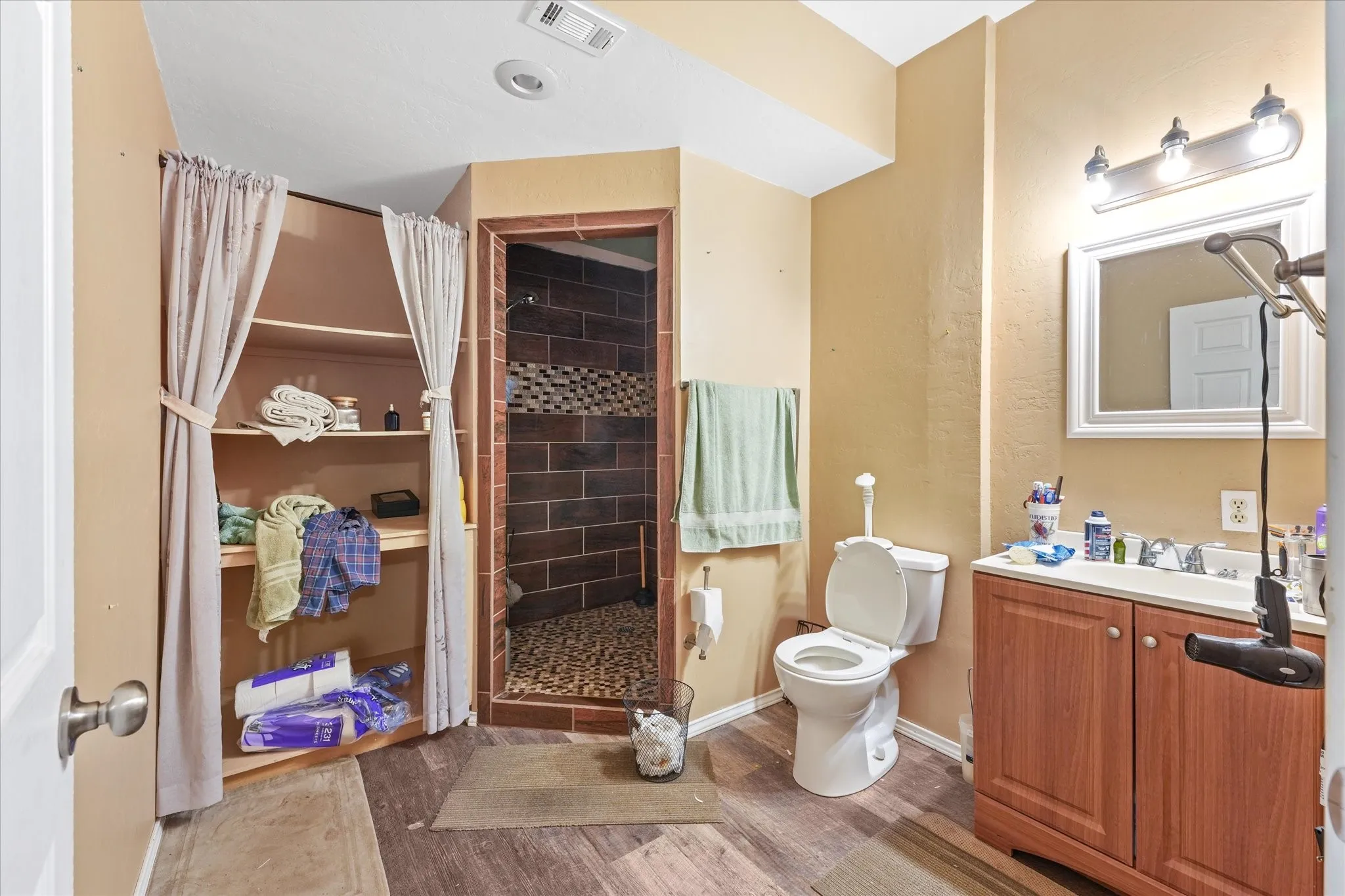 Full bathroom featuring a walk-in shower with stone tile and river rock flooring, wood-finish flooring, a vanity with a white sink, and a framed wall mirror
